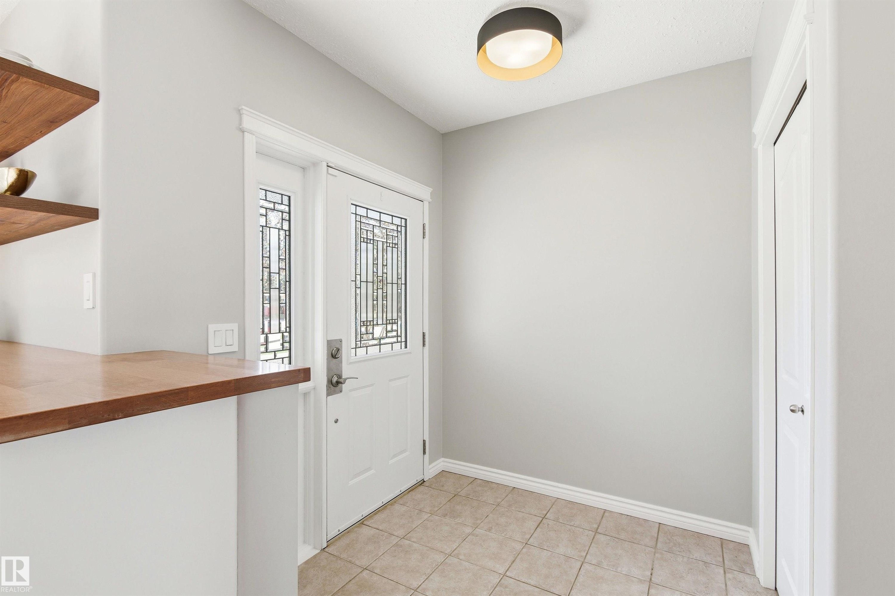 Entryway featuring a white door with decorative glass inserts, ceramic tile flooring, a built-in wood-finish shelf system, and a modern ceiling light fixture - 8730 92A Avenue, Edmonton, AB - Indoor Photo Showing Other Room