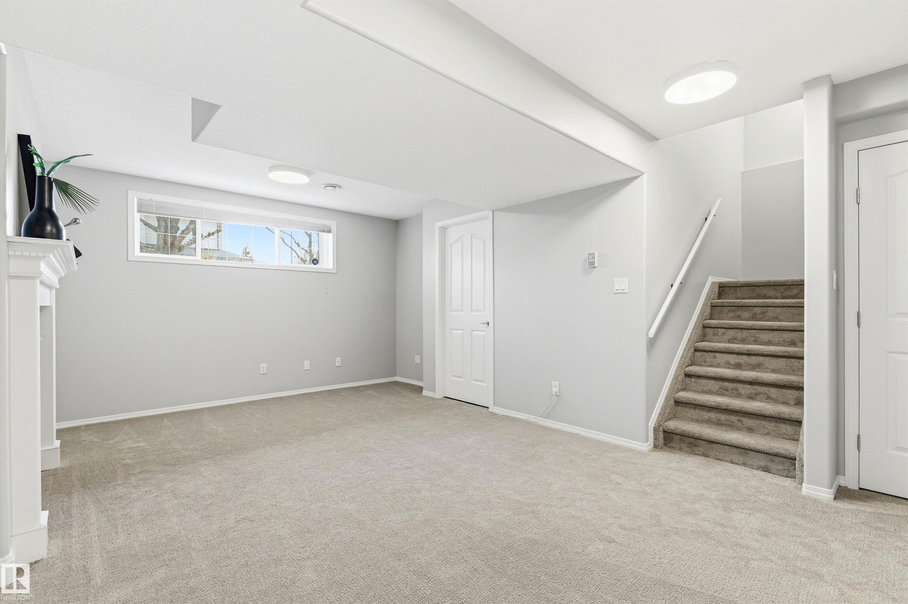 Finished basement living area featuring neutral carpeting, a white mantel, and a horizontal window - 8730 92A Avenue, Edmonton, AB - Indoor