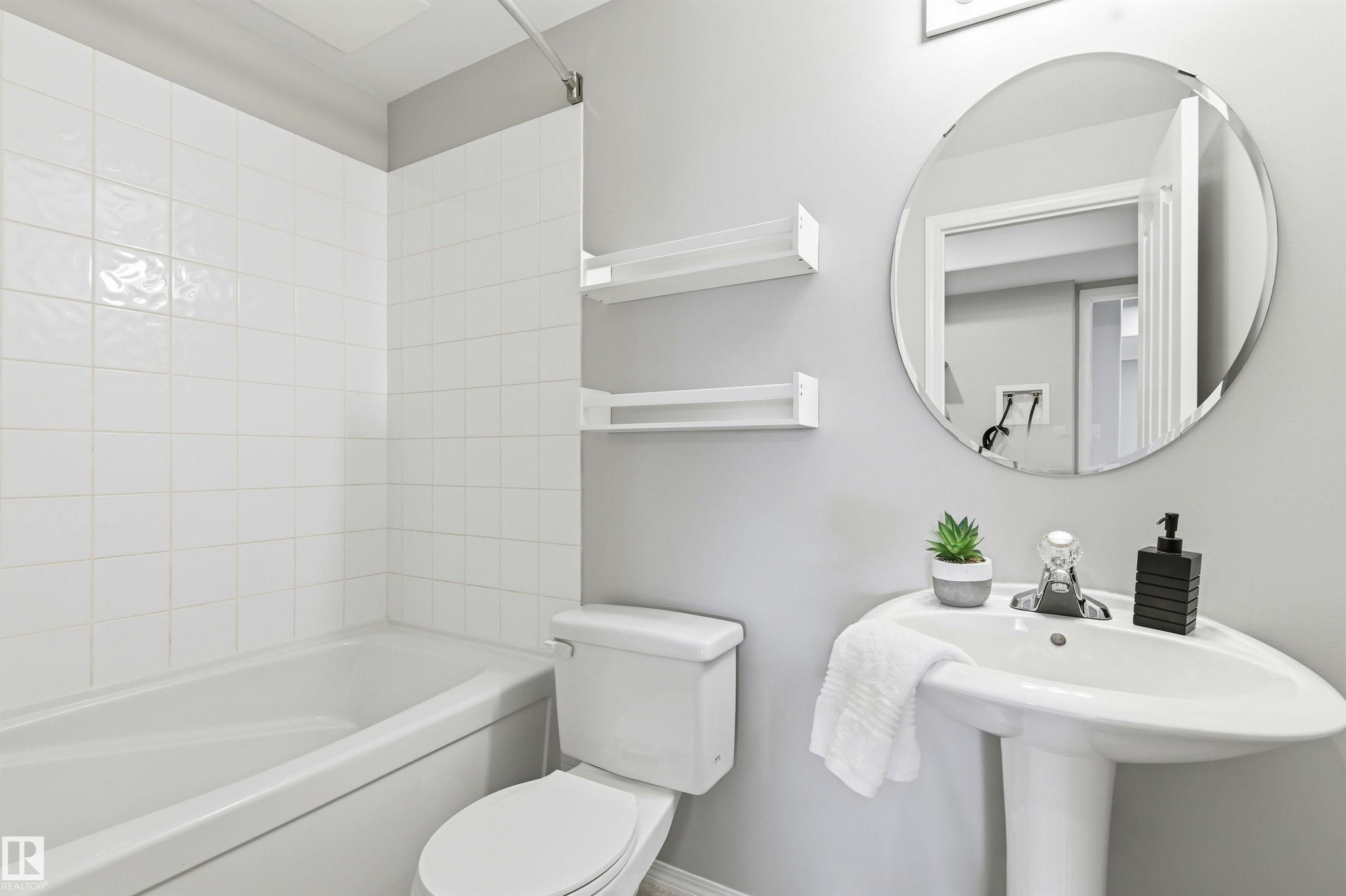 Bathroom featuring a white pedestal sink, a round wall-mounted mirror, and a white toilet - 8730 92A Avenue, Edmonton, AB - Indoor Photo Showing Bathroom