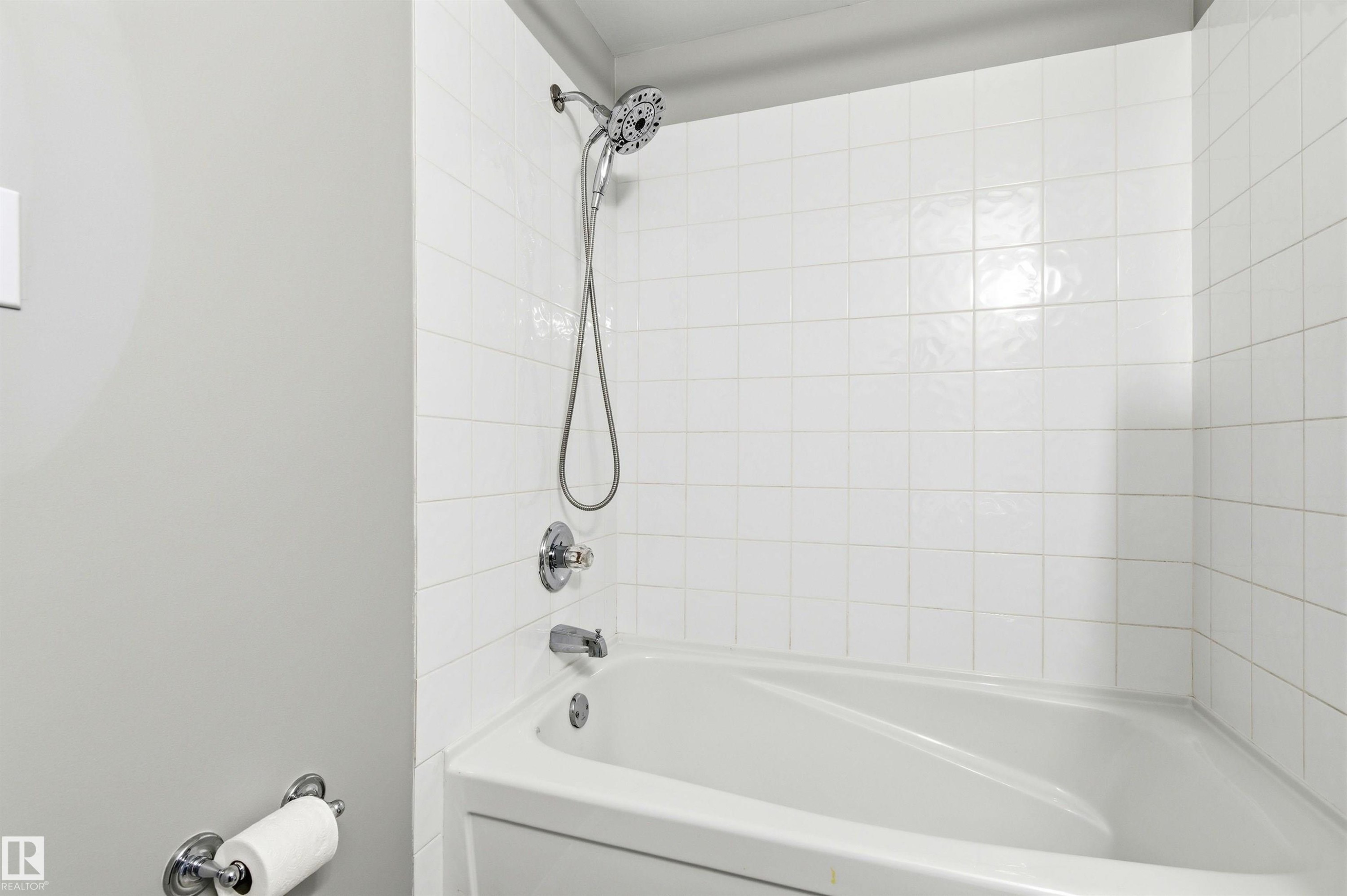 Tub and shower combination featuring white square tile surround, chrome fixtures, a handheld showerhead, and a integrated tub - 8730 92A Avenue, Edmonton, AB - Indoor Photo Showing Bathroom
