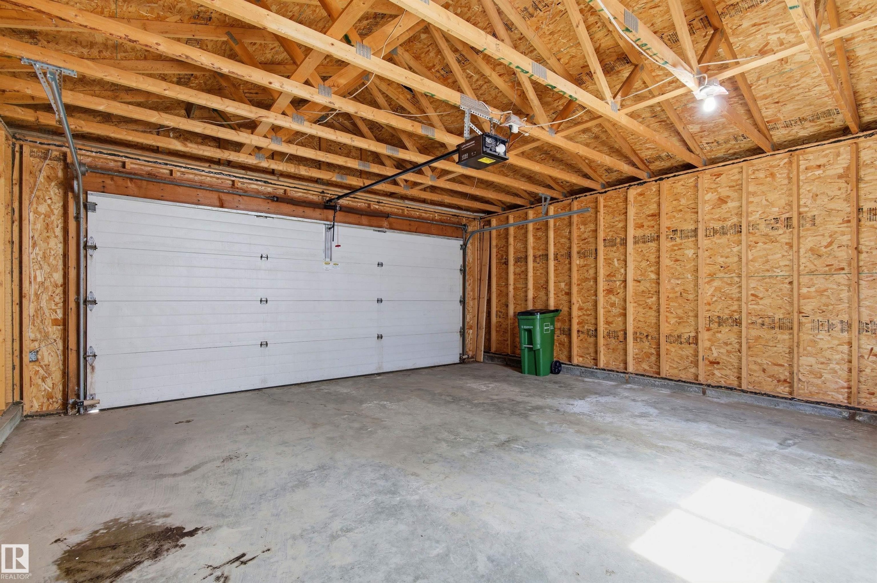 Attached garage featuring an automatic overhead door, exposed wooden ceiling trusses, concrete flooring, and unfinished wood panel walls - 8730 92A Avenue, Edmonton, AB - Indoor Photo Showing Garage