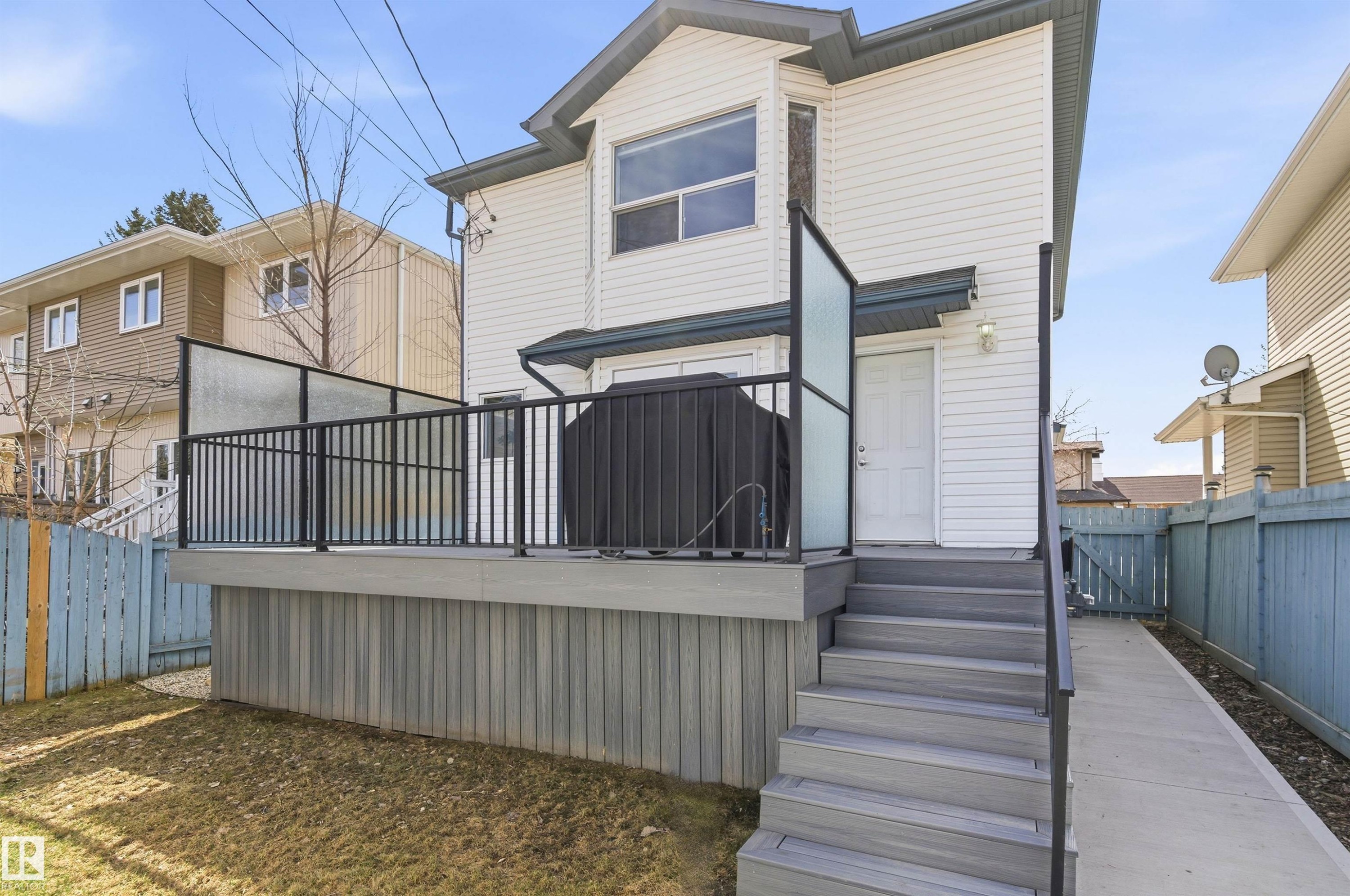 Rear exterior featuring white horizontal siding, a composite deck with black metal railings and privacy screens, and exterior lighting - 8730 92A Avenue, Edmonton, AB - Outdoor With Exterior