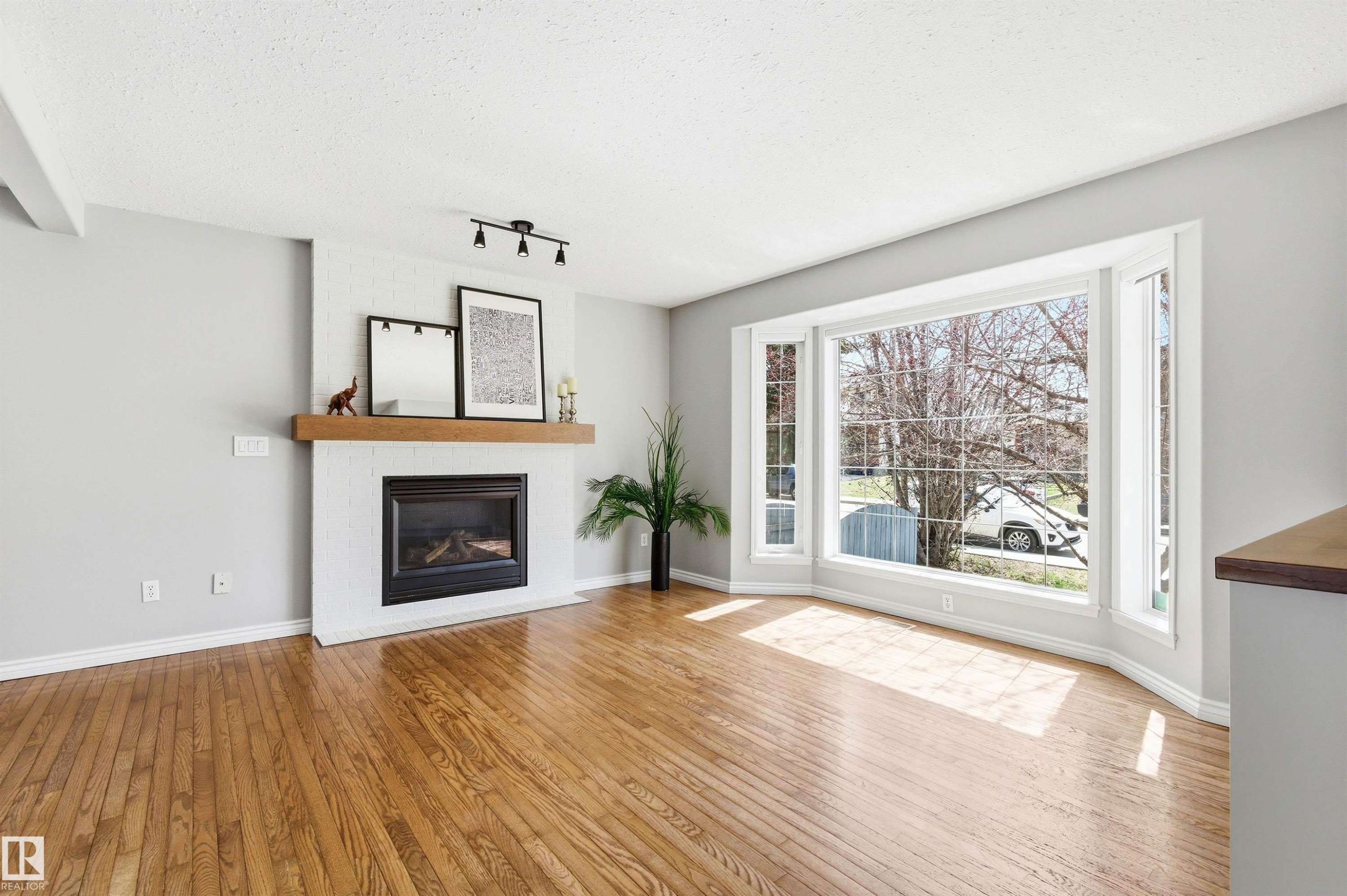 Expansive bay window illuminating wood-finish flooring - 8730 92A Avenue, Edmonton, AB - Indoor Photo Showing Living Room With Fireplace