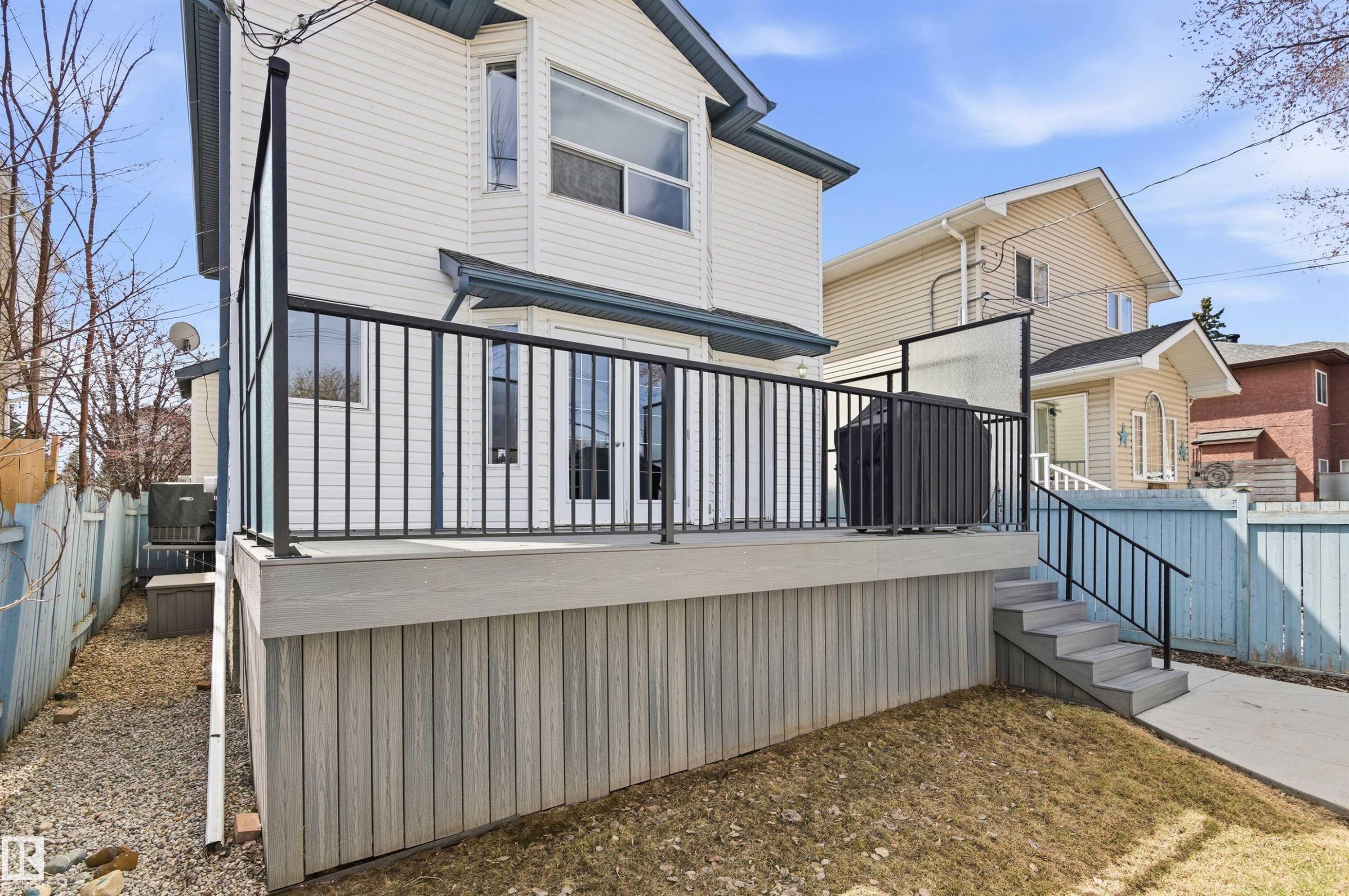 Rear exterior featuring a composite deck with black metal railings, leading to a concrete pathway - 8730 92A Avenue, Edmonton, AB - Outdoor With Exterior