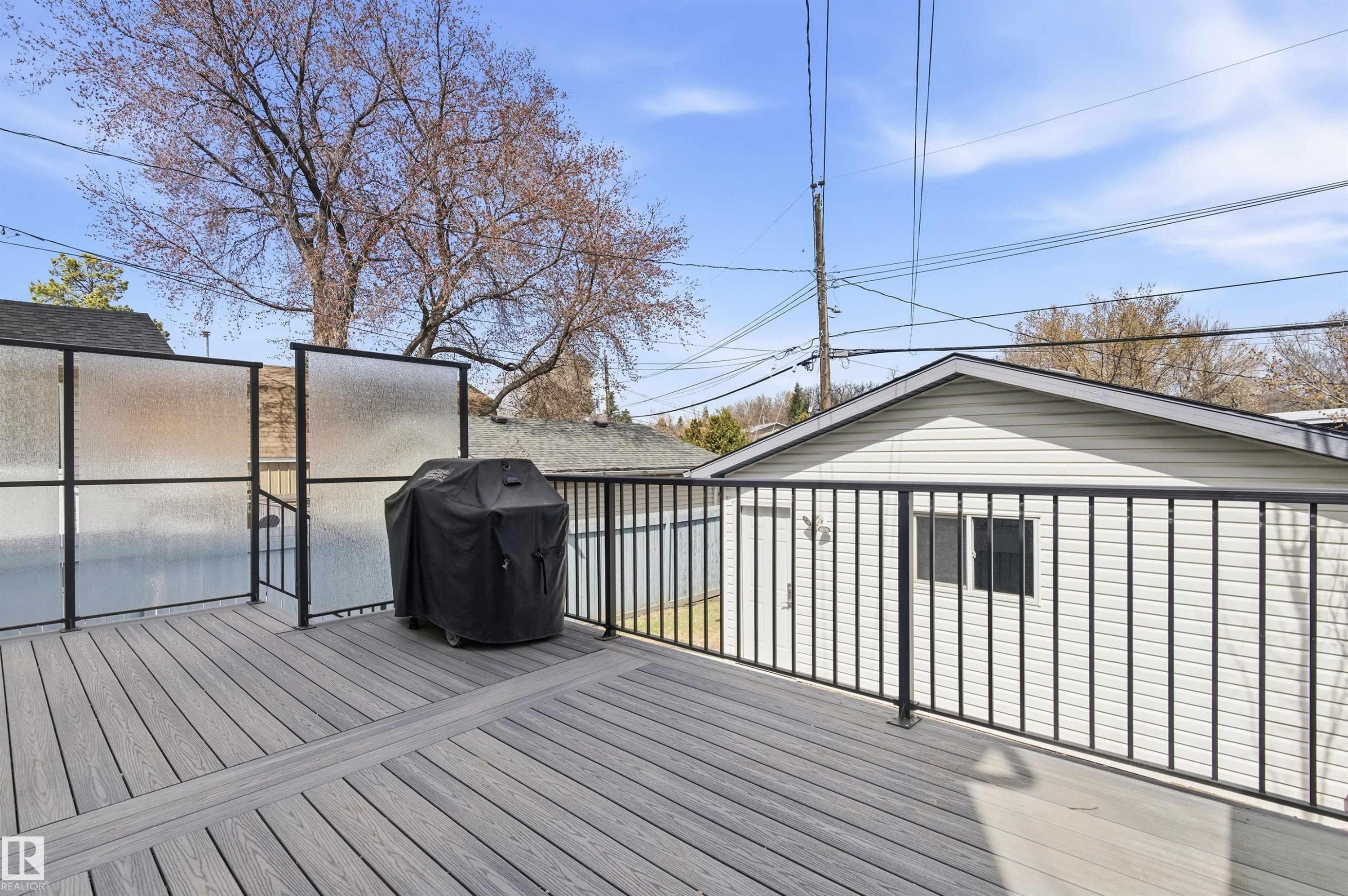 Expansive outdoor deck featuring composite decking, black metal railings, and frosted privacy screens - 8730 92A Avenue, Edmonton, AB - Outdoor