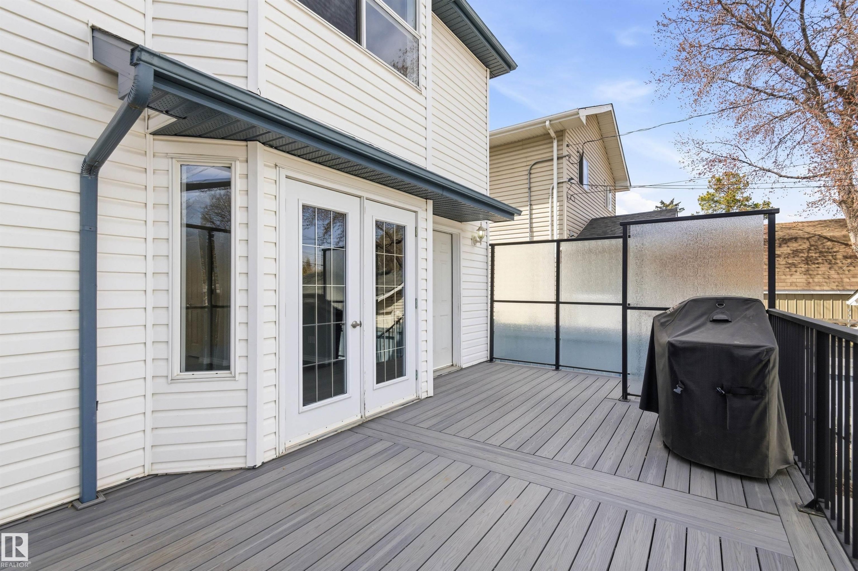 Spacious outdoor deck featuring composite decking, black metal railings, and a privacy screen - 8730 92A Avenue, Edmonton, AB - Outdoor With Exterior