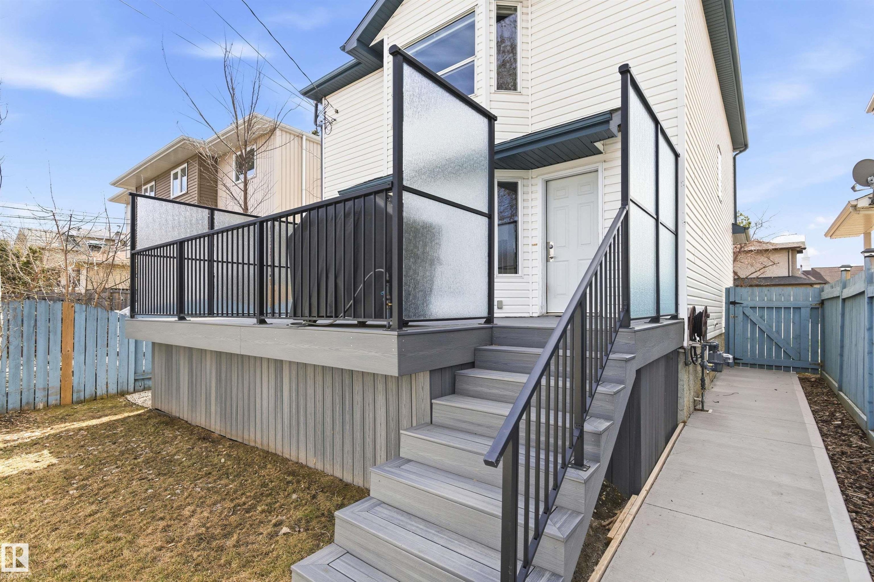 Raised exterior deck featuring composite decking, frosted glass privacy panels, black metal railings, and a concrete ramp for accessibility - 8730 92A Avenue, Edmonton, AB - Outdoor With Deck Patio Veranda With Exterior
