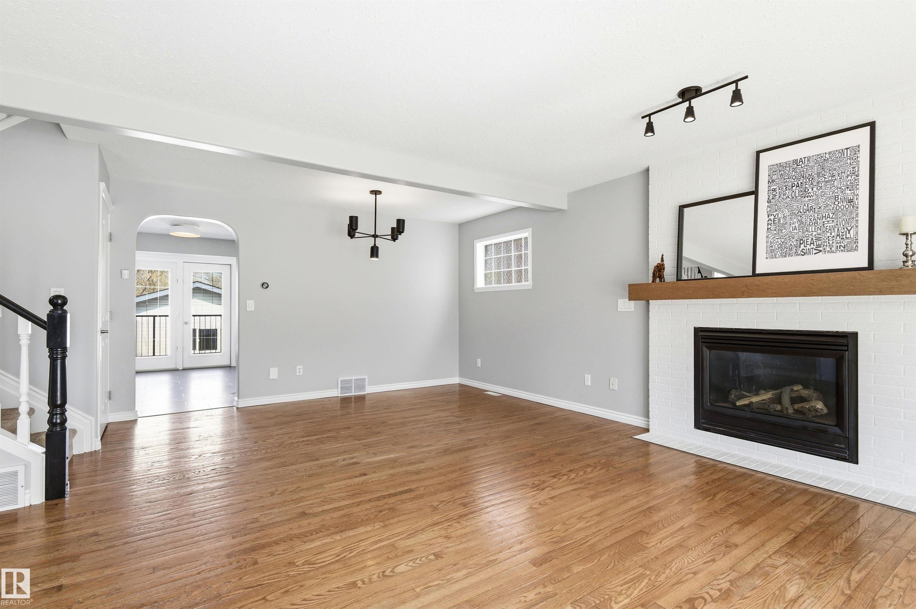 Spacious living area featuring polished wood-finish flooring, a white tiled fireplace with a wood-beam mantel, and recessed window - 8730 92A Avenue, Edmonton, AB - Indoor Photo Showing Living Room With Fireplace