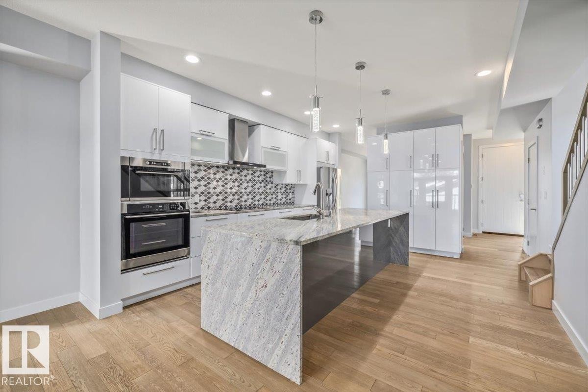 Kitchen featuring a large center island with a stone countertop, integrated sink, and modern pendant lighting - 8706 88 Avenue, Edmonton, AB - Indoor Photo Showing Kitchen With Upgraded Kitchen