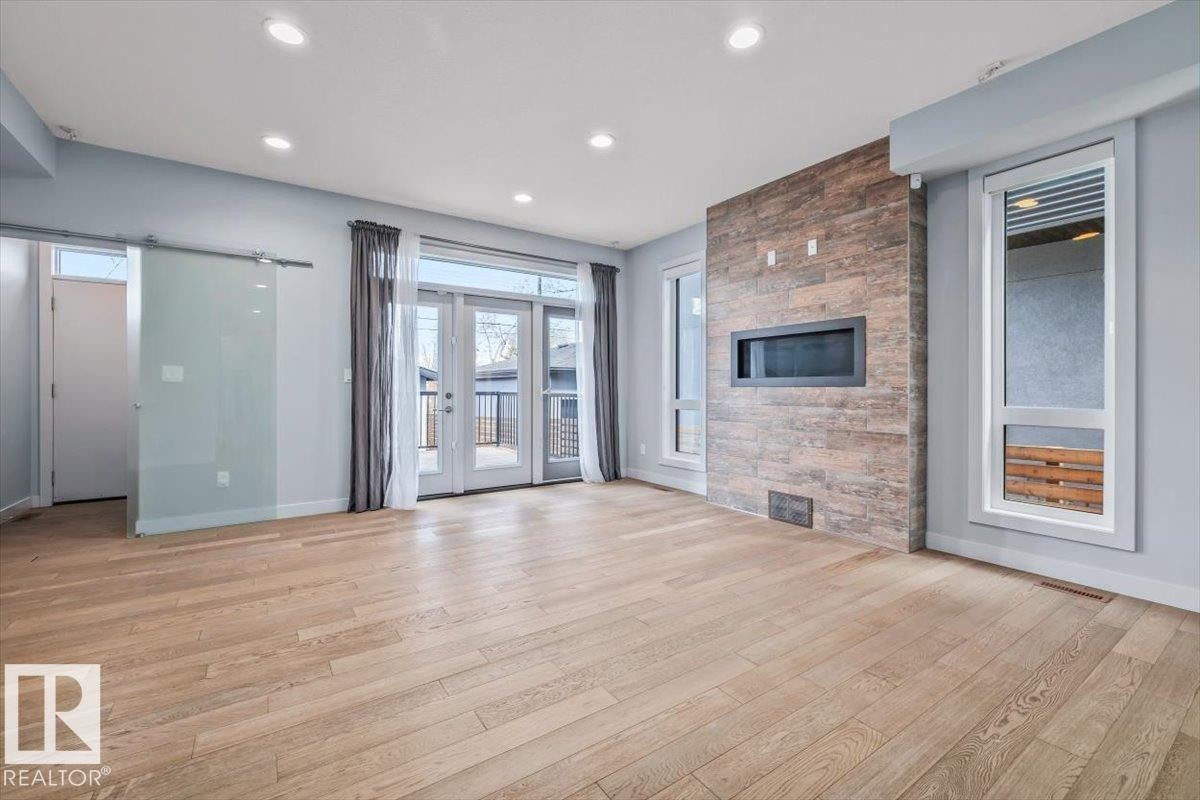 Spacious room featuring wood-finish flooring, recessed lighting, and a modern fireplace with a textured surround - 8706 88 Avenue, Edmonton, AB - Indoor With Fireplace