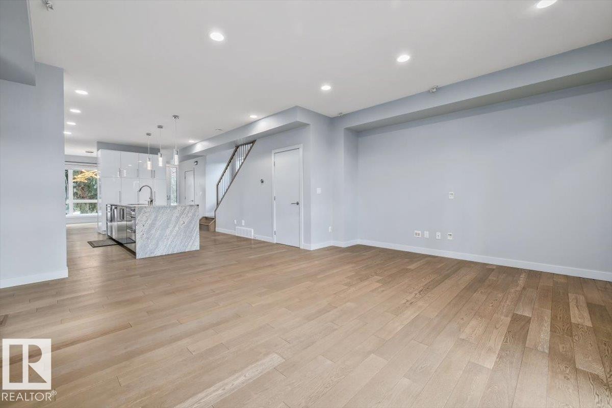 Open-concept living space with light wood-finish flooring, recessed ceiling lighting, and a kitchen island featuring a waterfall countertop - 8706 88 Avenue, Edmonton, AB - Indoor Photo Showing Other Room