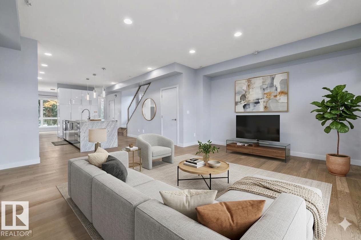 Open-concept living area featuring wood-finish flooring, recessed lighting, a modern staircase with dark railing, and a kitchen island with stone waterfall edge - 8706 88 Avenue, Edmonton, AB - Indoor Photo Showing Living Room