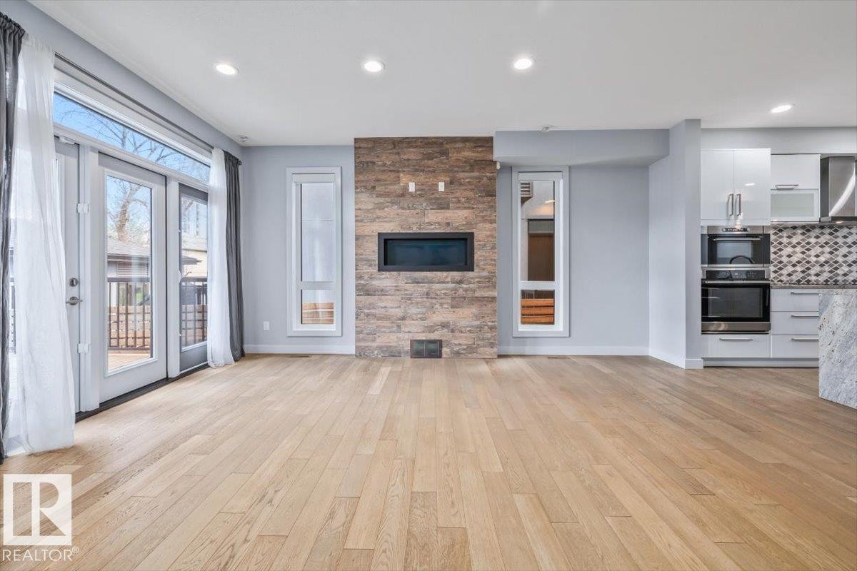 Open-concept living space featuring wood-finish flooring, a contemporary fireplace with a stone-clad surround, and recessed lighting - 8706 88 Avenue, Edmonton, AB - Indoor With Fireplace