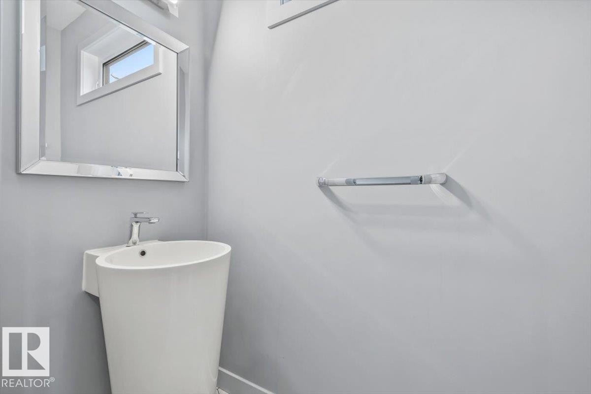 Pedestal sink with a single-handle chrome faucet, rectangular framed mirror, light gray wall paint, and a chrome towel bar - 8706 88 Avenue, Edmonton, AB - Indoor Photo Showing Bathroom