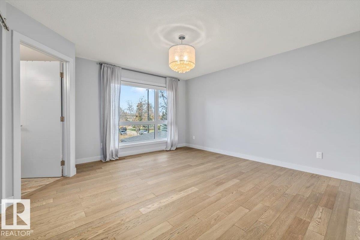 Spacious room featuring wood-finish flooring, a large window, a decorative ceiling light fixture, and a solid-core interior door - 8706 88 Avenue, Edmonton, AB - Indoor Photo Showing Other Room