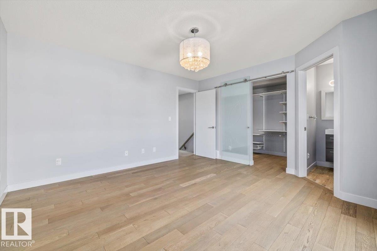 Light wood-finish flooring, a contemporary chandelier, a custom closet with built-in shelving, a frosted glass barn door, and a full bathroom with a single vanity - 8706 88 Avenue, Edmonton, AB - Indoor Photo Showing Other Room