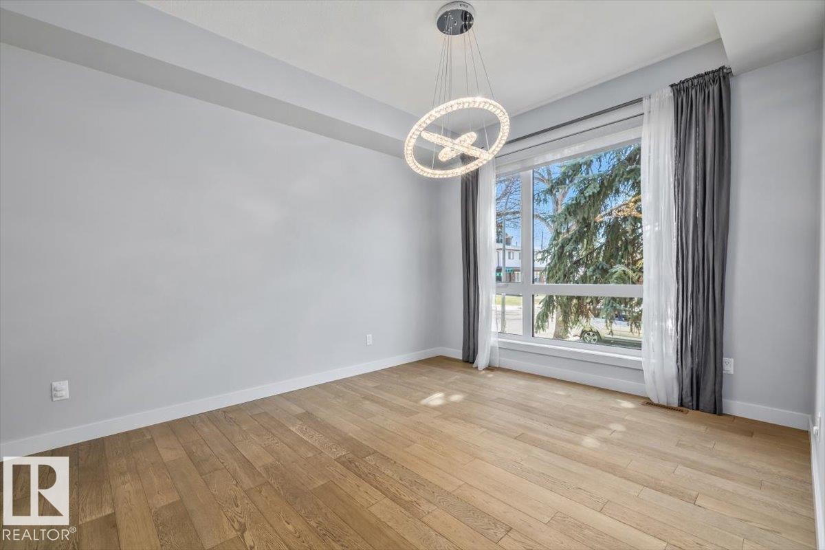 Spacious room featuring wood-finish flooring, a large multi-pane window, and a contemporary chandelier - 8706 88 Avenue, Edmonton, AB - Indoor Photo Showing Other Room