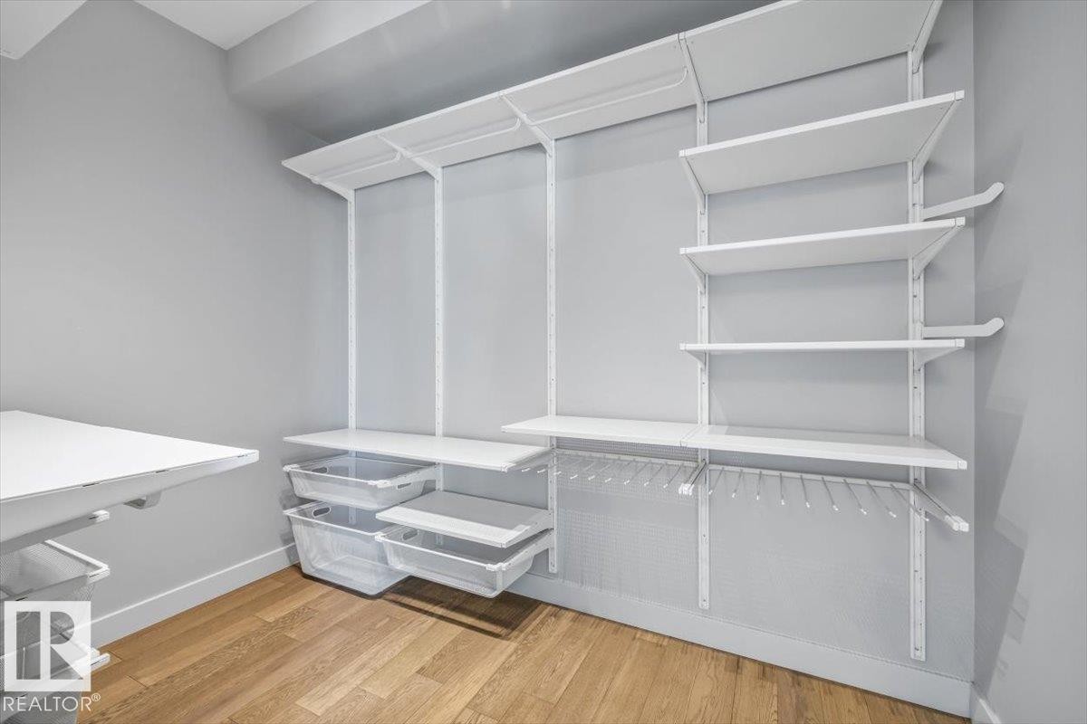 Customizable closet system with wood-finish flooring, white shelving, hanging storage, and pull-out storage bins - 8706 88 Avenue, Edmonton, AB - Indoor With Storage