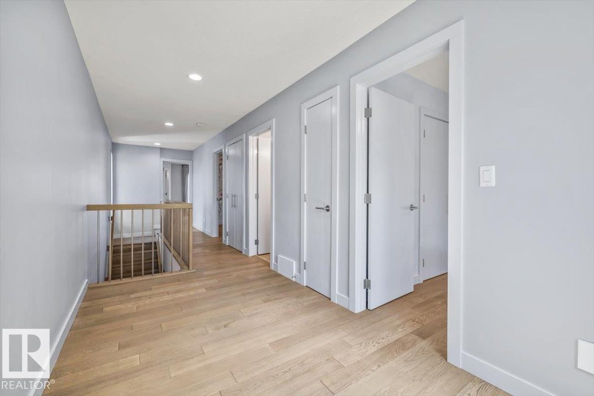 Hallway featuring wood-finish flooring, recessed lighting, light gray wall paint, white trim, and a wood railing - 8706 88 Avenue, Edmonton, AB - Indoor Photo Showing Other Room