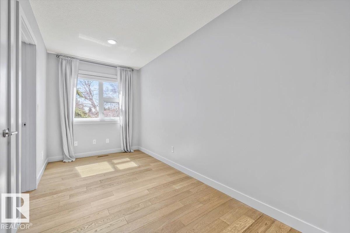 Bright interior room featuring a large window with white trim, wood-finish flooring, recessed lighting, and a solid interior door with brushed nickel hardware - 8706 88 Avenue, Edmonton, AB - Indoor Photo Showing Other Room