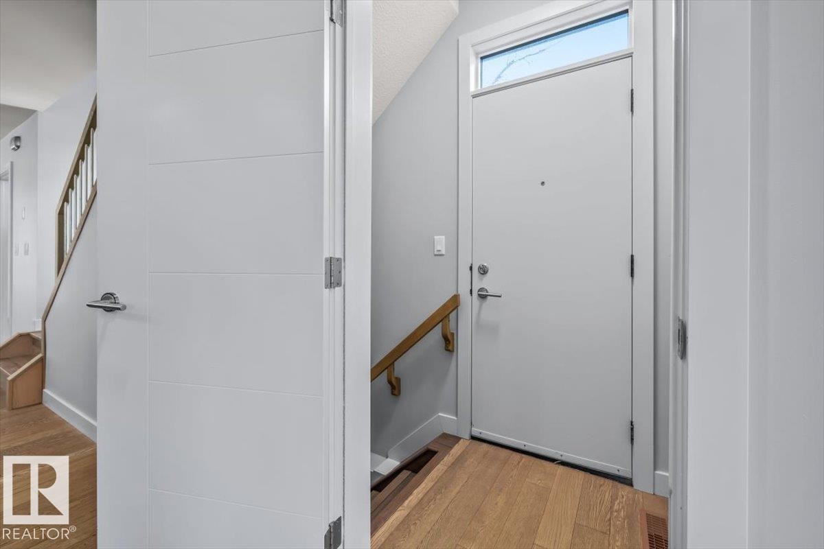 Side entryway featuring a white door with transom window, wood-finish flooring, and a wood handrail - 8706 88 Avenue, Edmonton, AB - Indoor Photo Showing Other Room