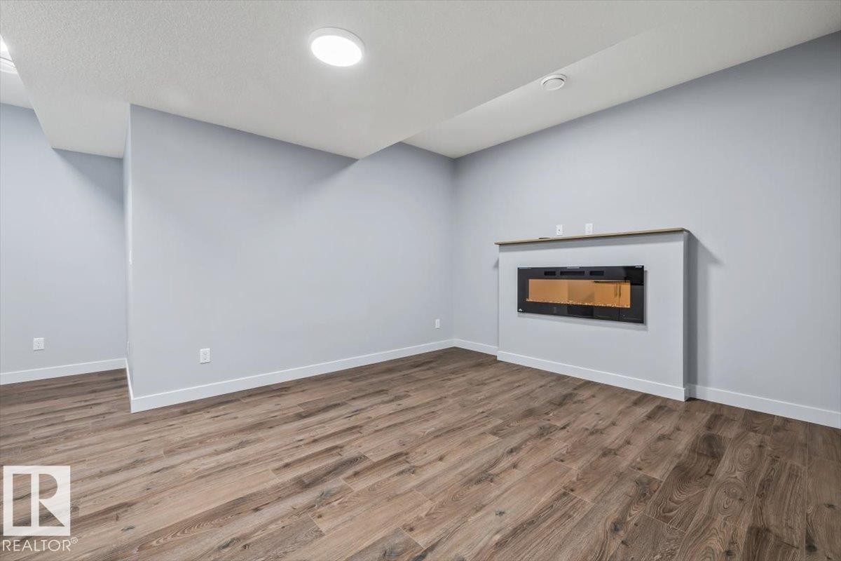 Spacious interior with wood-finish flooring, light gray walls, white baseboards, recessed ceiling lighting, and a built-in electric fireplace with a wood-finish mantel - 8706 88 Avenue, Edmonton, AB - Indoor With Fireplace