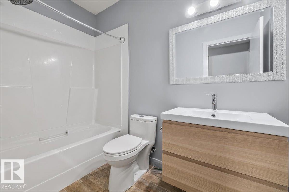 Contemporary bathroom featuring a white tub and shower surround, a sleek toilet, and wood-finish vanity with an integrated sink - 8706 88 Avenue, Edmonton, AB - Indoor Photo Showing Bathroom