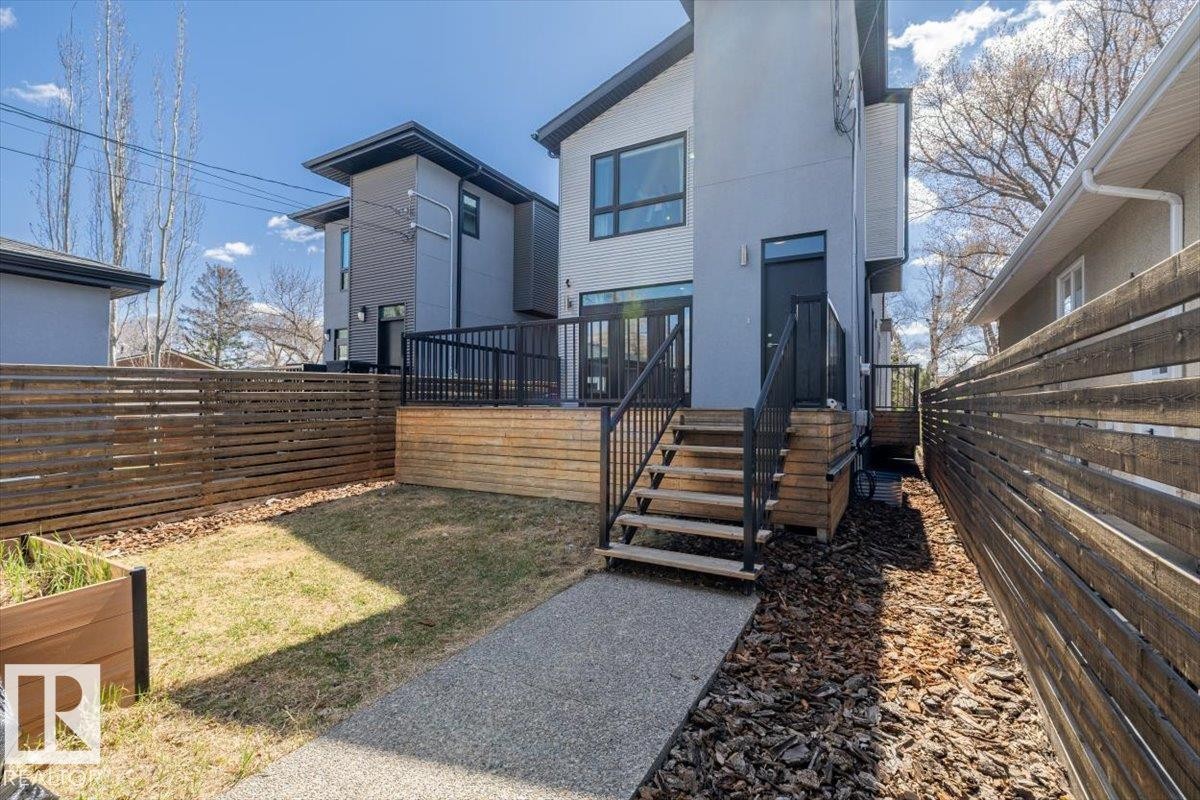 Rear exterior featuring a raised wooden deck with black railings, a gravel pathway, and horizontal slatted fencing - 8706 88 Avenue, Edmonton, AB - Outdoor