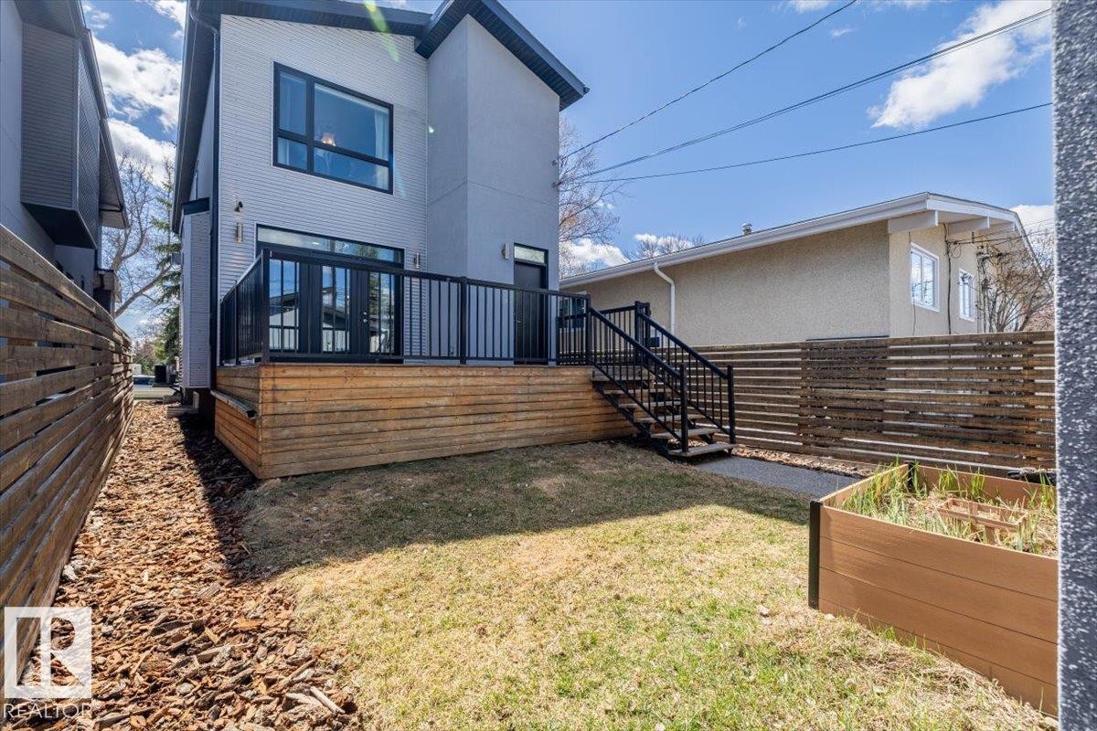 Rear exterior featuring a spacious wood deck with black railings, double patio doors, and exterior stairs - 8706 88 Avenue, Edmonton, AB - Outdoor With Exterior