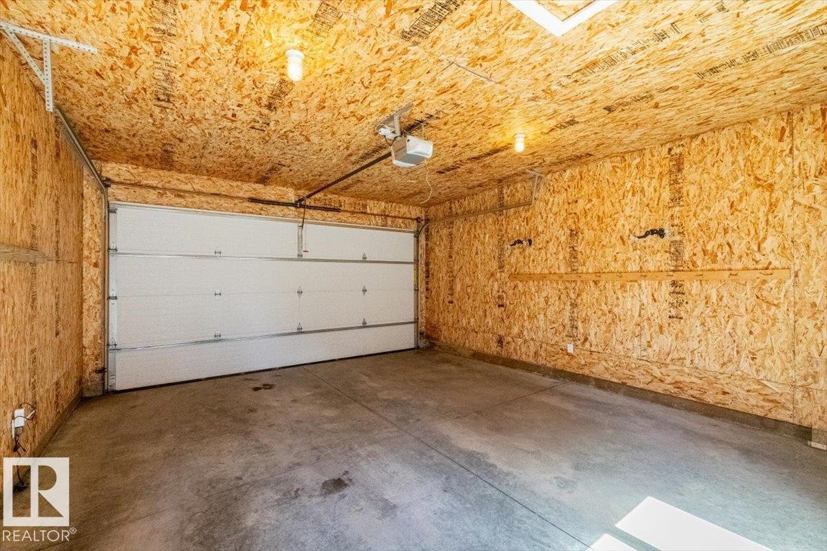 Attached garage with a white sectional door, concrete flooring, and oriented strand board walls - 8706 88 Avenue, Edmonton, AB - Indoor Photo Showing Garage