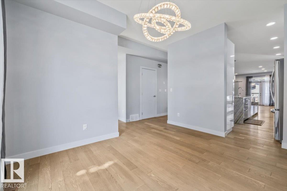 Expansive wood-finish flooring extends throughout the space, complemented by a contemporary chandelier light fixture - 8706 88 Avenue, Edmonton, AB - Indoor Photo Showing Other Room