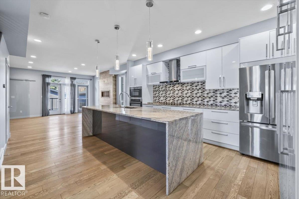 Open-concept kitchen and living area featuring wood-finish flooring, a large island with a stone countertop, white cabinetry, and stainless steel appliances - 8706 88 Avenue, Edmonton, AB - Indoor Photo Showing Kitchen With Stainless Steel Kitchen With Upgraded Kitchen