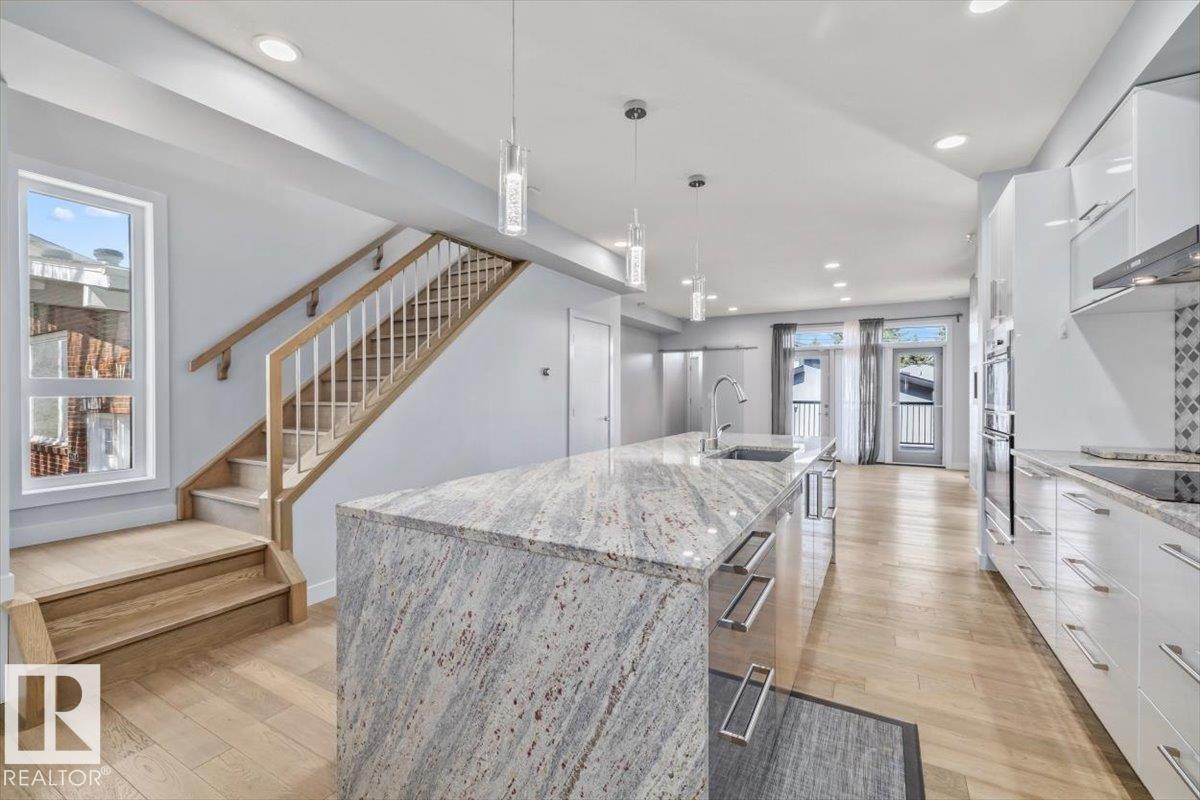 Contemporary kitchen featuring a large island with an integrated sink and pendant lighting, light wood-finish flooring, white cabinetry, a tiled backsplash, and recessed lighting - 8706 88 Avenue, Edmonton, AB - Indoor Photo Showing Kitchen With Upgraded Kitchen