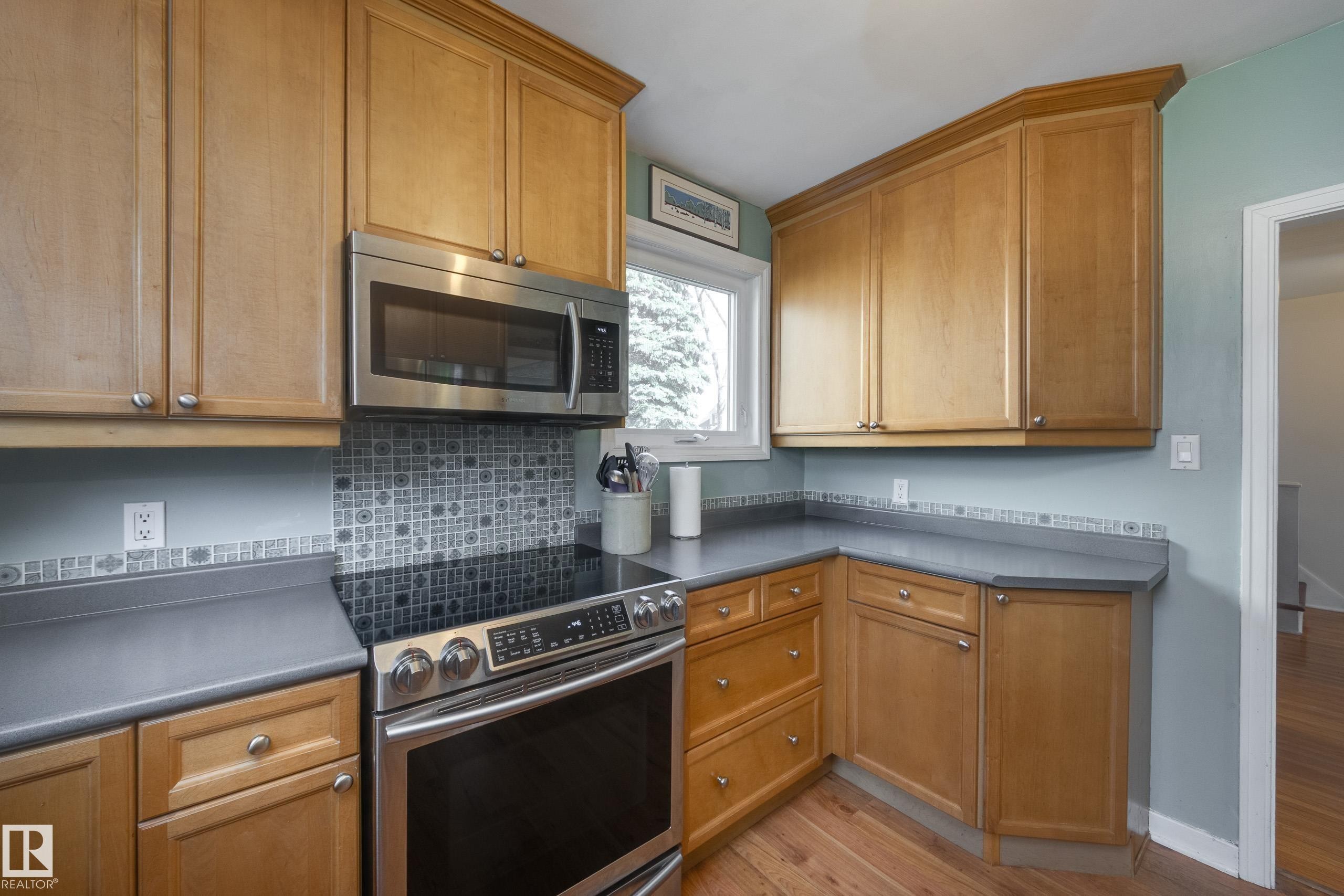 Kitchen featuring light wood cabinetry, a stainless steel over-the-range microwave, a glass-top electric range, a gray countertop, and a decorative tile backsplash - 11516 72 Avenue, Edmonton, AB - Indoor Photo Showing Kitchen