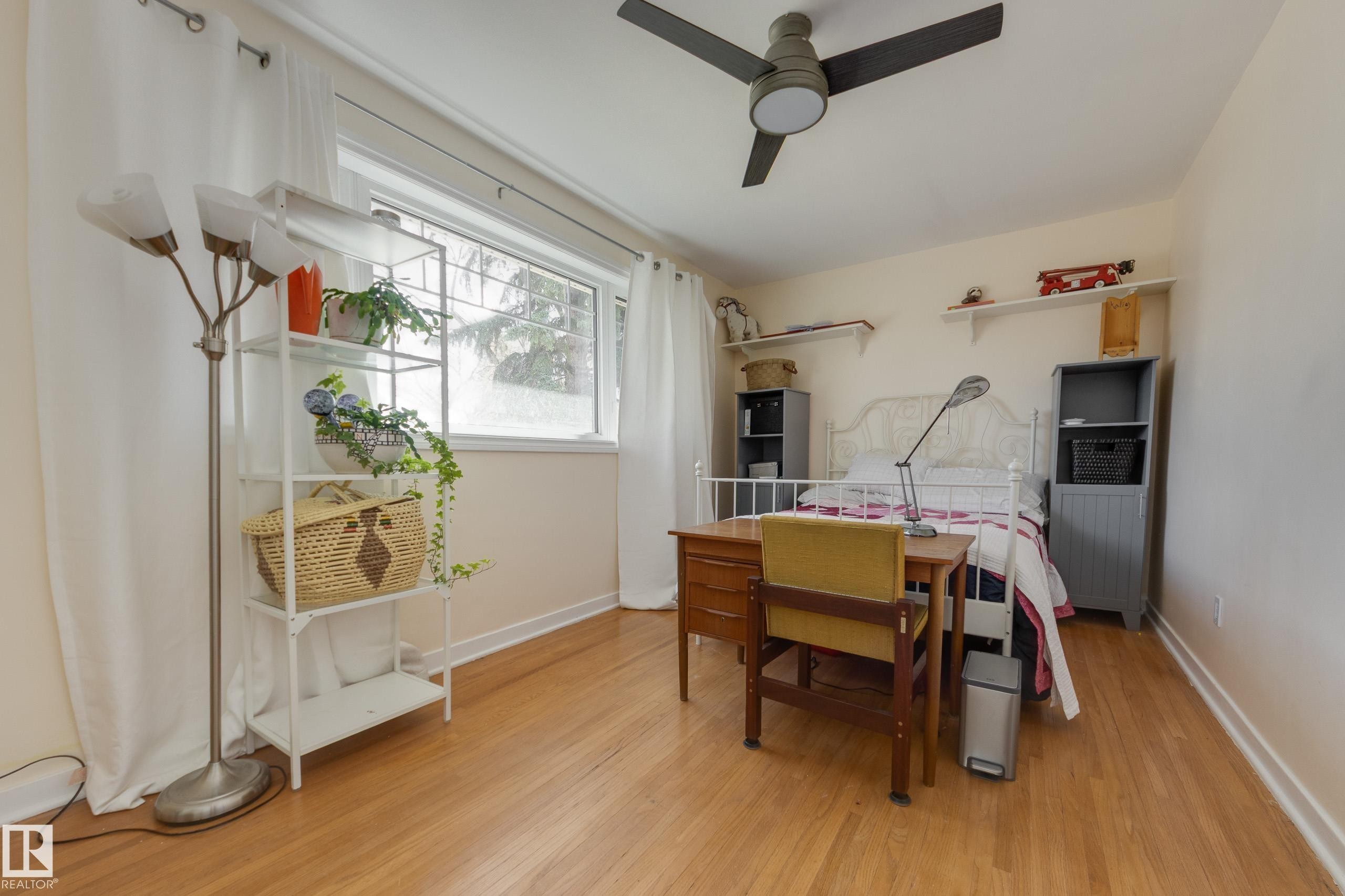 Hardwood-style flooring extends throughout this room, featuring a ceiling fan, a large window, and light-colored walls - 11516 72 Avenue, Edmonton, AB - Indoor