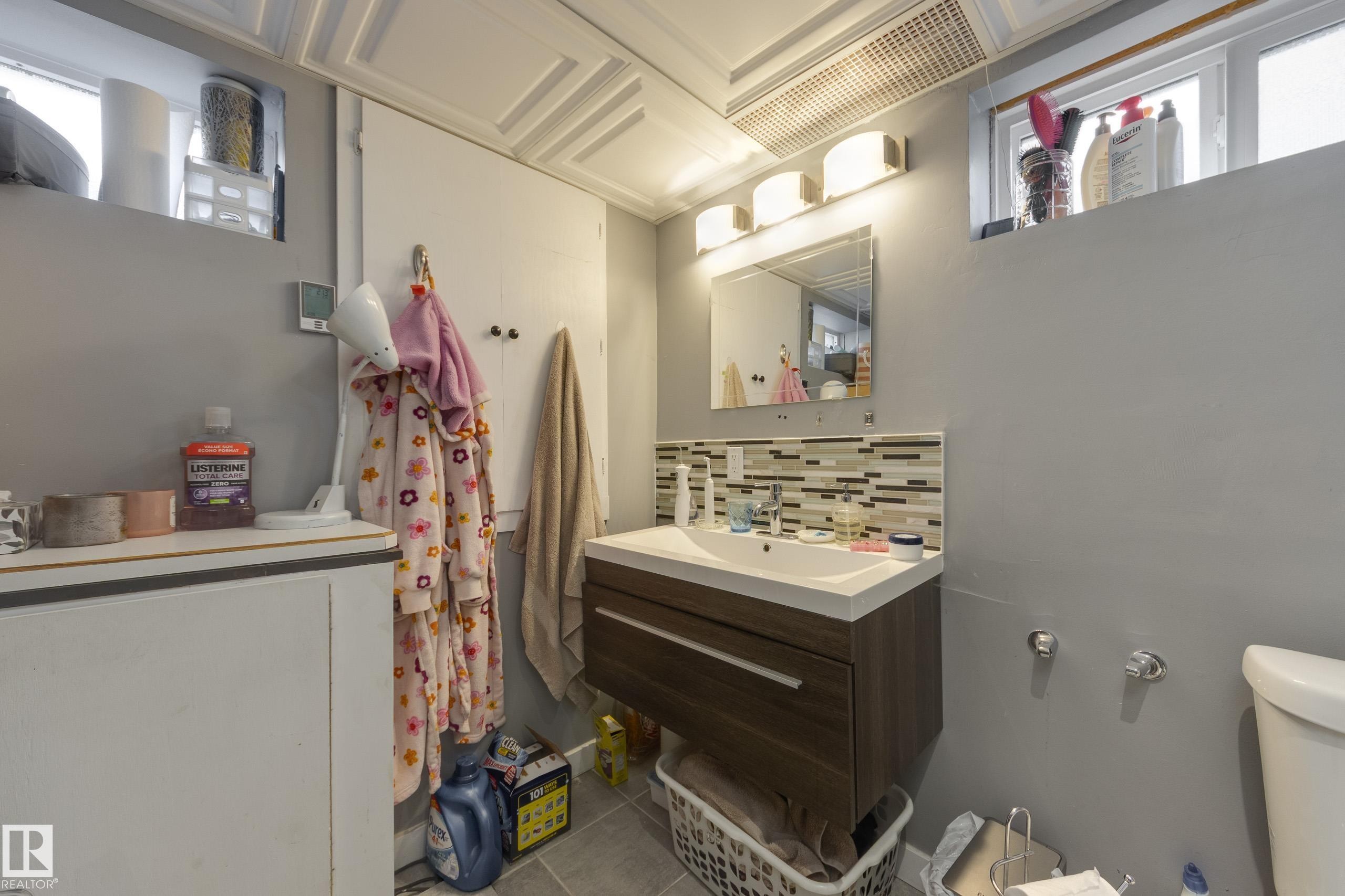 Modern bathroom featuring a floating wood-finish vanity with an integrated sink, a rectangular mirror, and an illuminated three-light fixture - 11516 72 Avenue, Edmonton, AB - Indoor Photo Showing Other Room