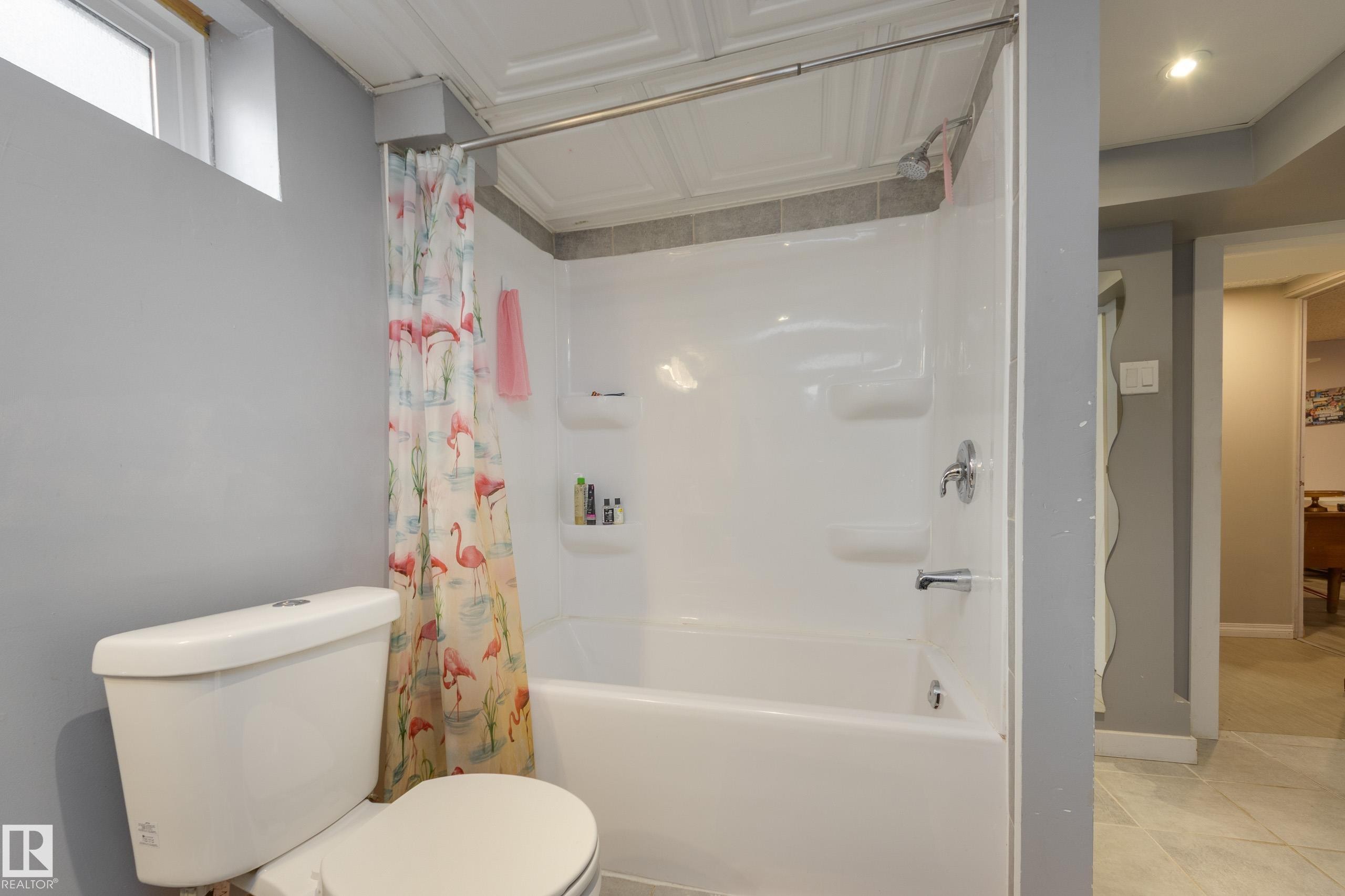 Bathroom featuring a white toilet, a shower-over-tub combination with integrated shelving, and a decorative ceiling panel - 11516 72 Avenue, Edmonton, AB - Indoor Photo Showing Bathroom