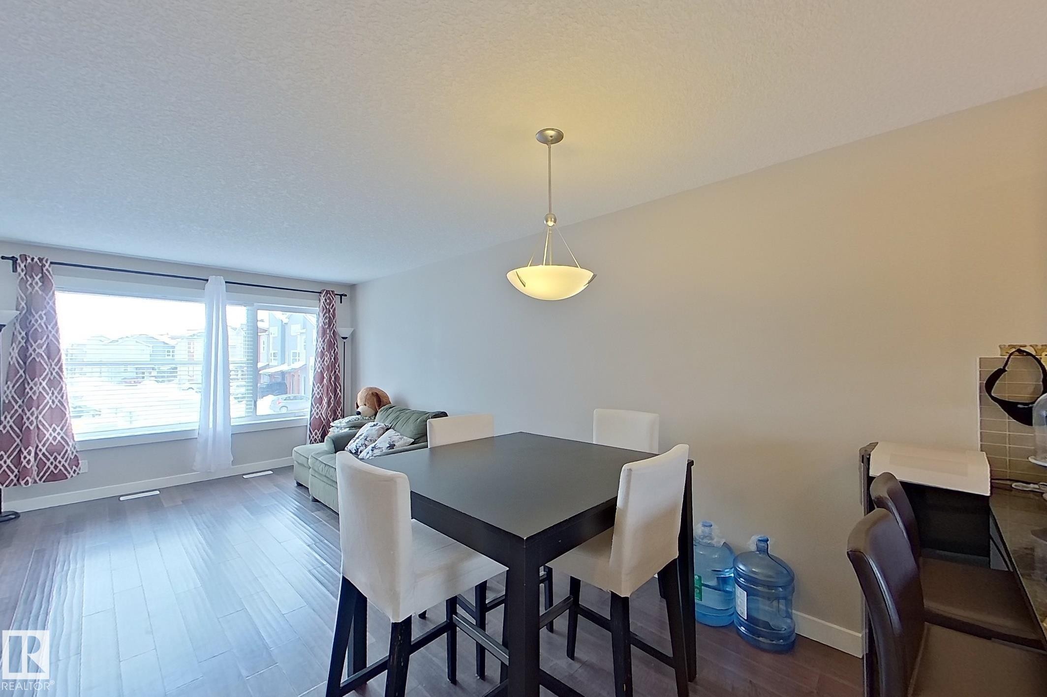 Open-concept living area featuring wood-finish flooring, a large window, a ceiling-mounted light fixture, and light-toned walls - 295 401 Southfork, Leduc, AB - Indoor Photo Showing Dining Room