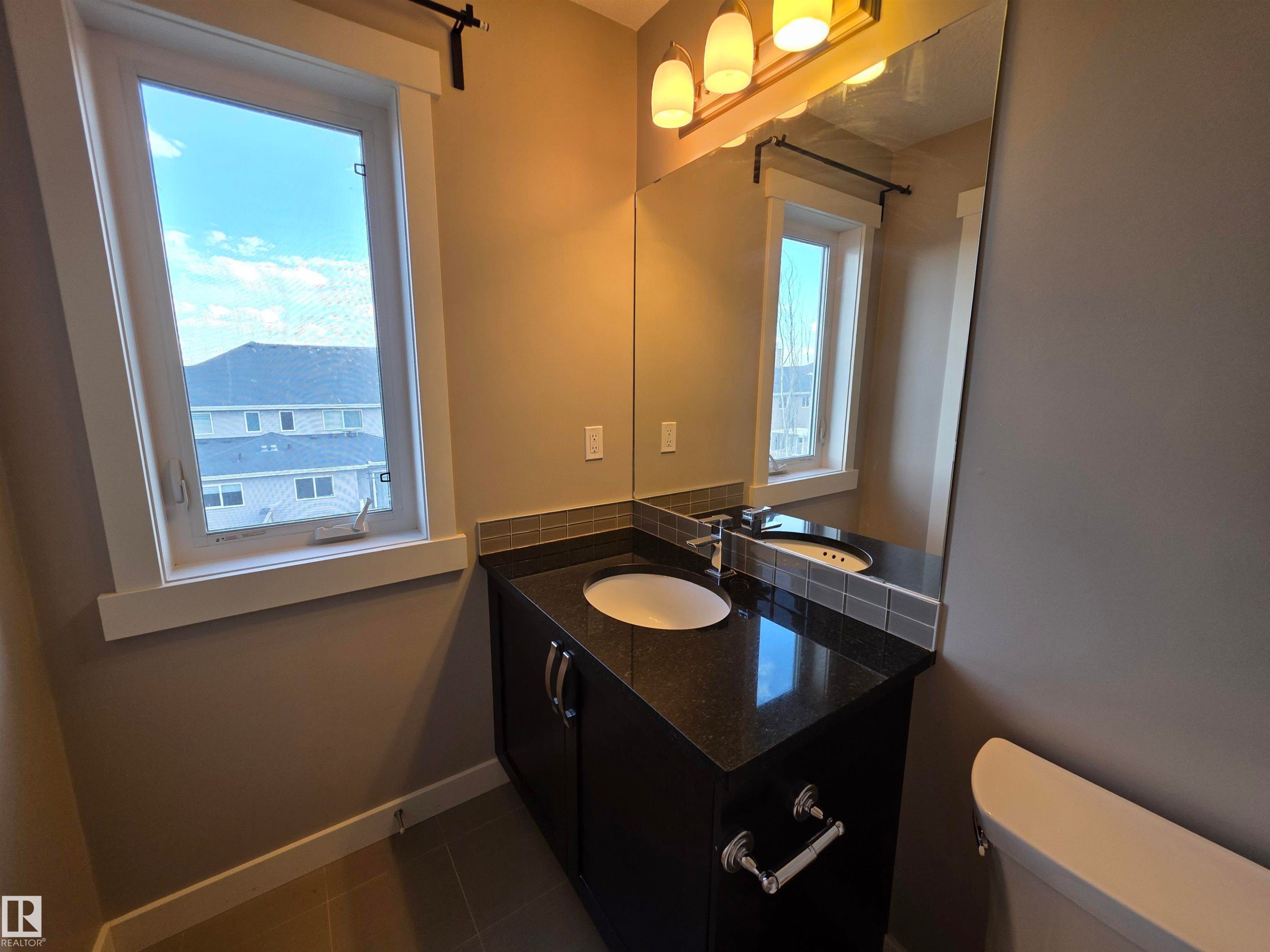 Vanity with a dark granite countertop, integrated white sink, and dark wood-finish cabinetry - 295 401 Southfork, Leduc, AB - Indoor Photo Showing Bathroom