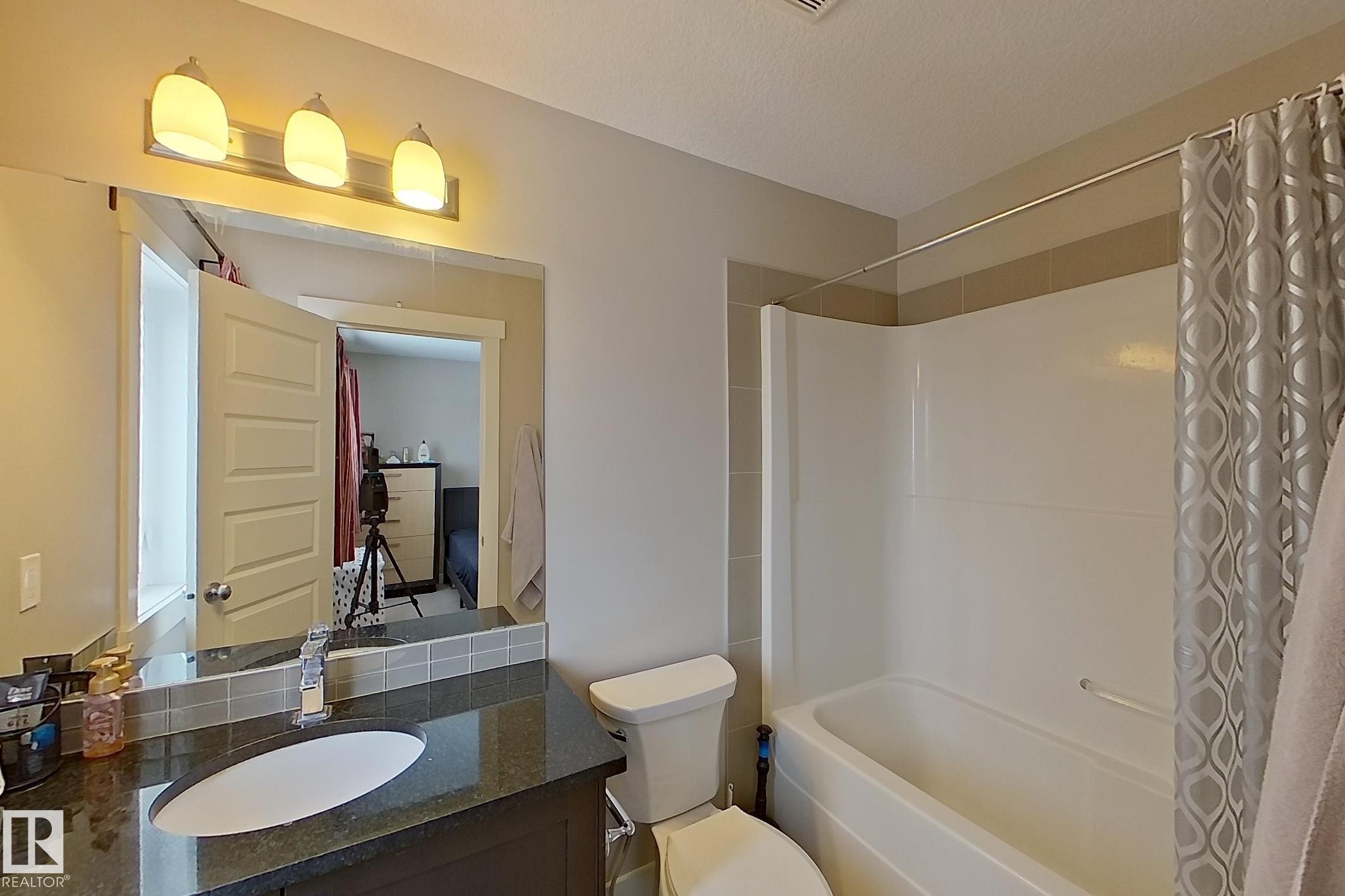 Bathroom featuring a shower/tub combination with white surround, a dark vanity with a polished countertop, an undermount sink, and a tiled backsplash - 295 401 Southfork, Leduc, AB - Indoor Photo Showing Bathroom