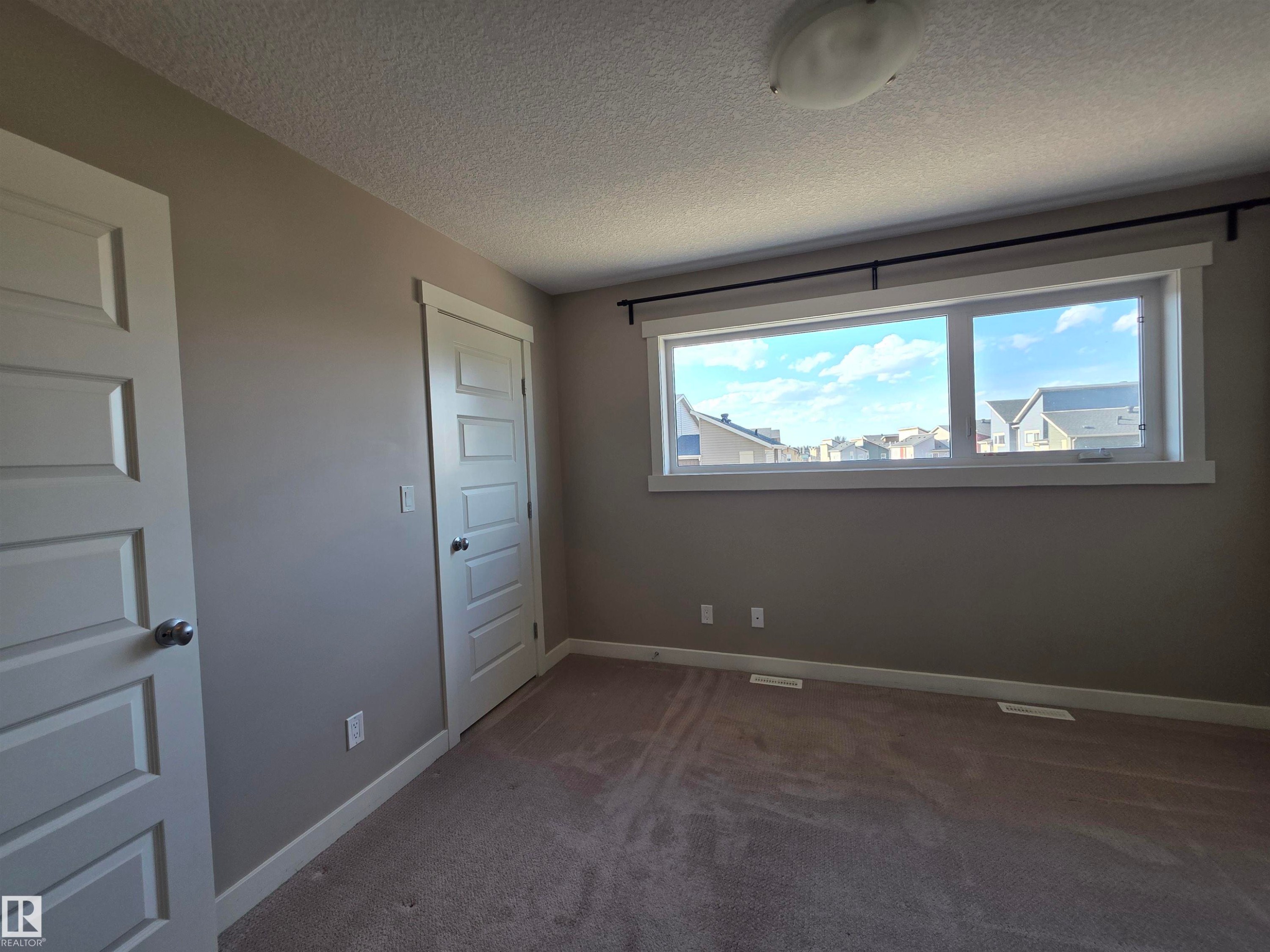 Bright interior space featuring a wide window with white trim, tan carpeting, and light gray walls - 295 401 Southfork, Leduc, AB - Indoor Photo Showing Other Room