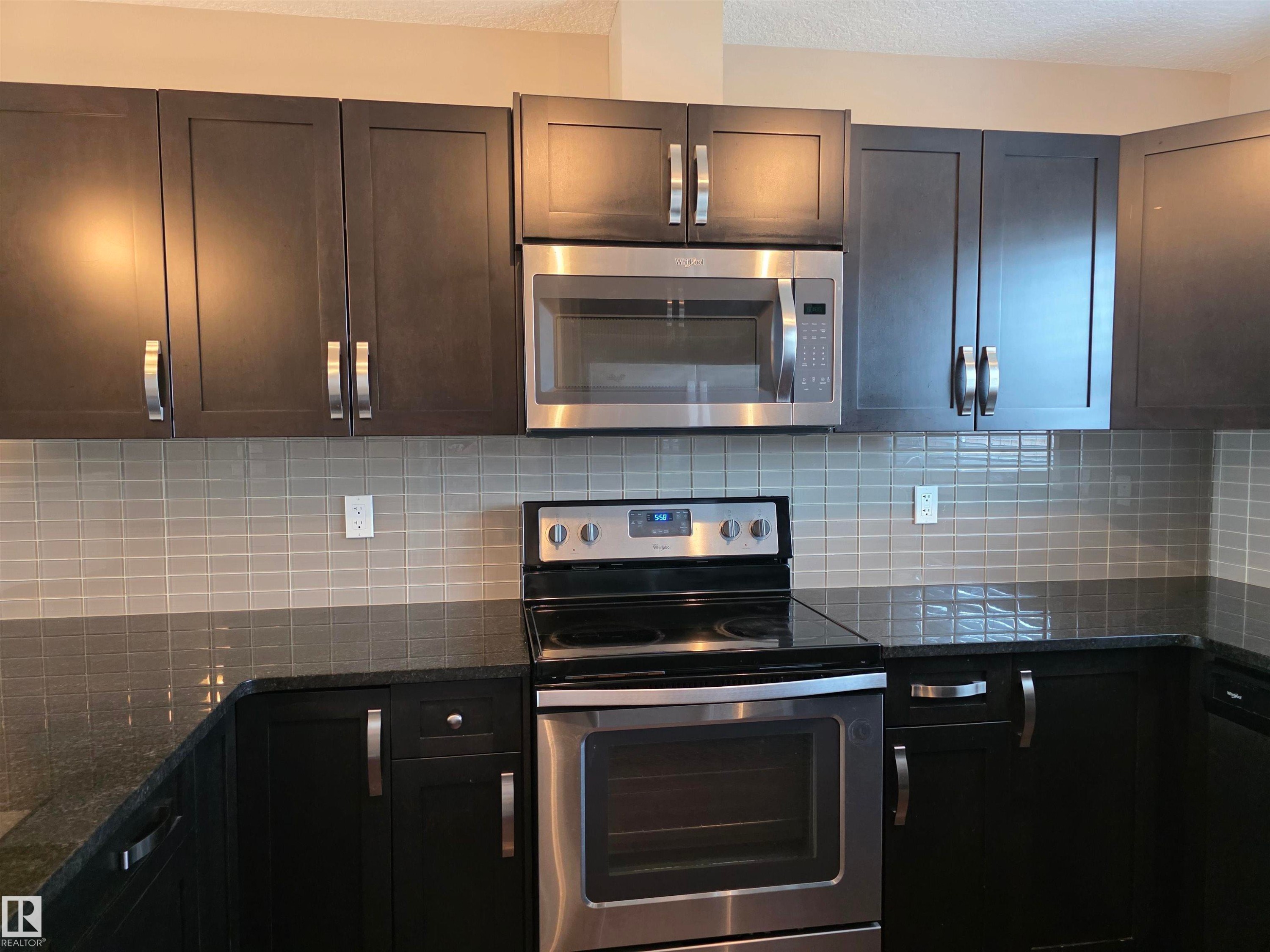 Kitchen featuring dark cabinetry, stainless steel appliances, a tile backsplash, and dark countertops - 295 401 Southfork, Leduc, AB - Indoor Photo Showing Kitchen With Upgraded Kitchen