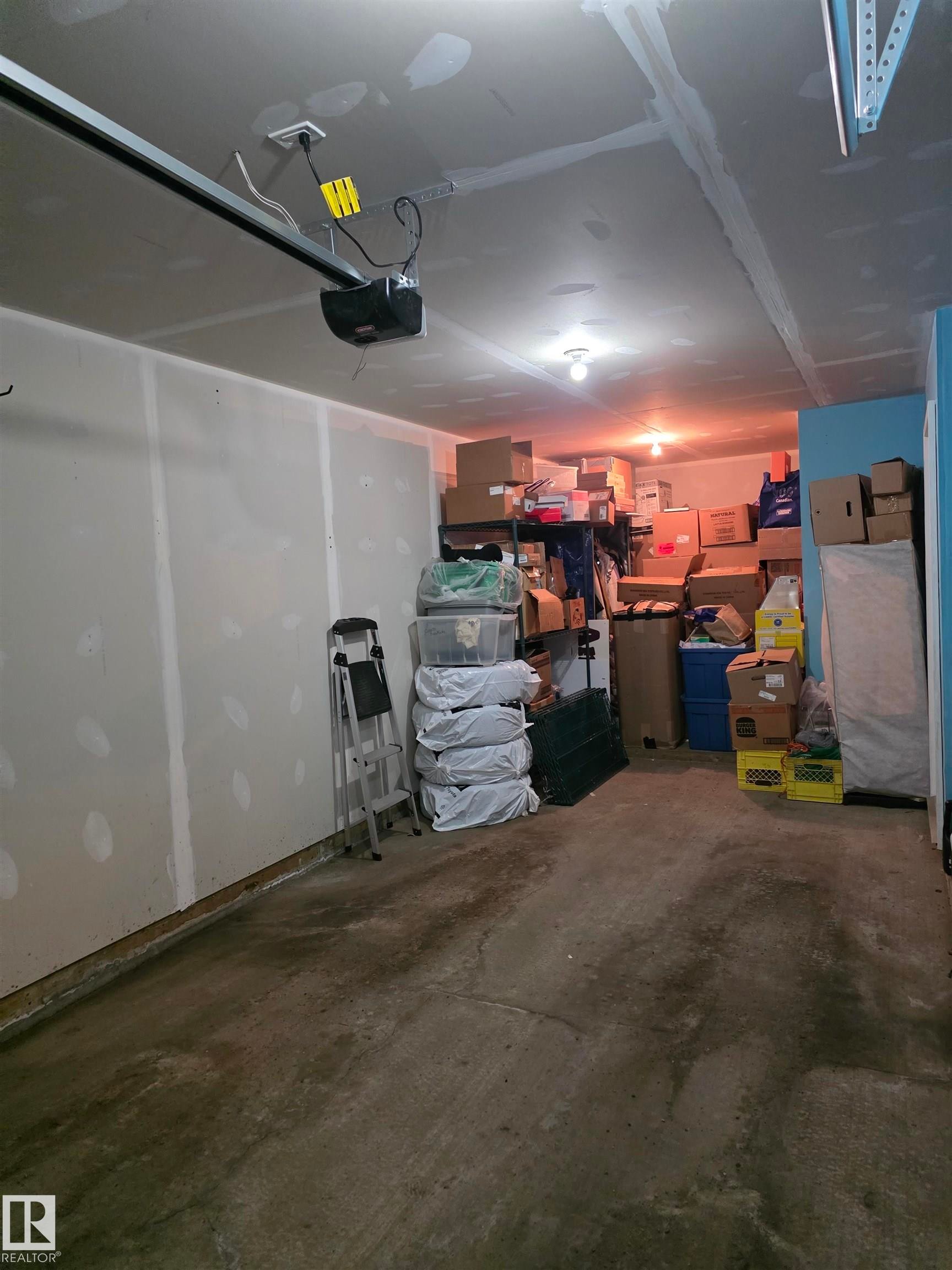 Unfinished garage space featuring a concrete floor, exposed drywall, and an overhead garage door opener - 295 401 Southfork, Leduc, AB - Indoor Photo Showing Garage