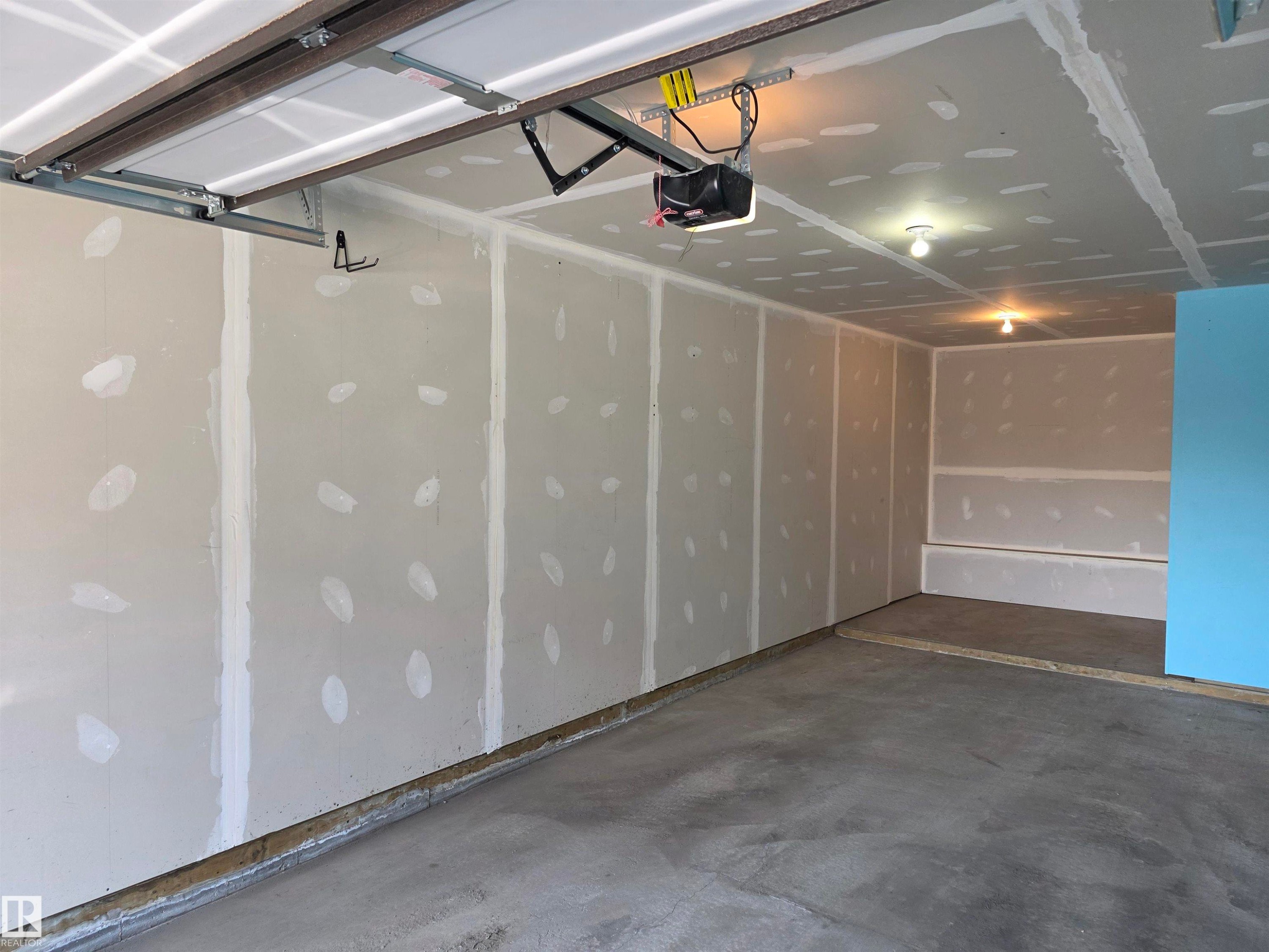 Garage space featuring an automatic opener system, exposed drywall, concrete flooring, and ceiling-mounted light fixtures - 295 401 Southfork, Leduc, AB - Indoor Photo Showing Garage