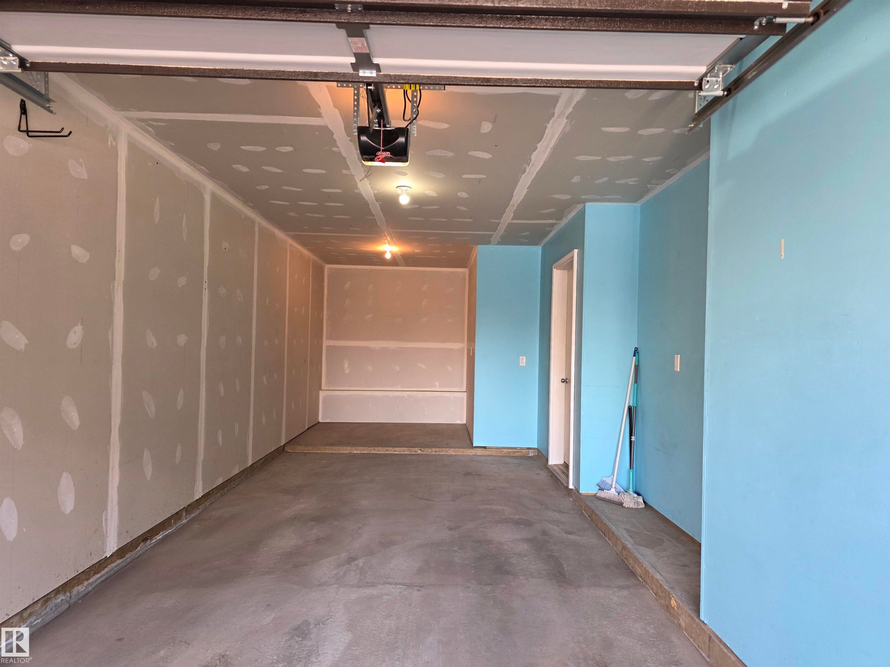 Concrete flooring in a spacious garage featuring drywall walls, a garage door opener, and integrated ceiling lighting - 295 401 Southfork, Leduc, AB - Indoor Photo Showing Garage