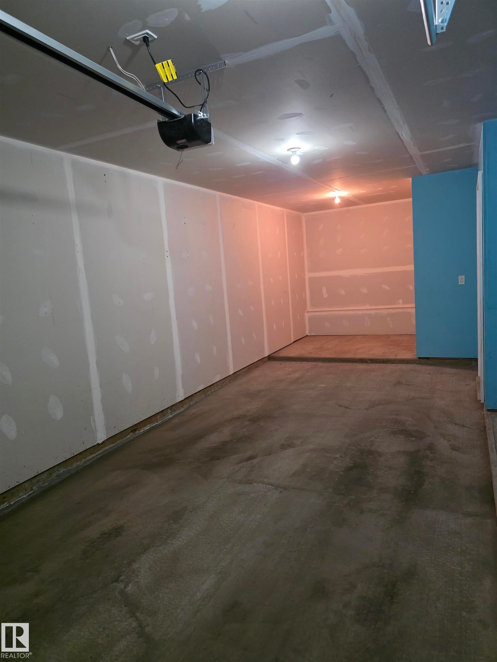 Spacious garage featuring a concrete floor, exposed drywall, and an installed garage door opener - 295 401 Southfork, Leduc, AB - Indoor Photo Showing Garage