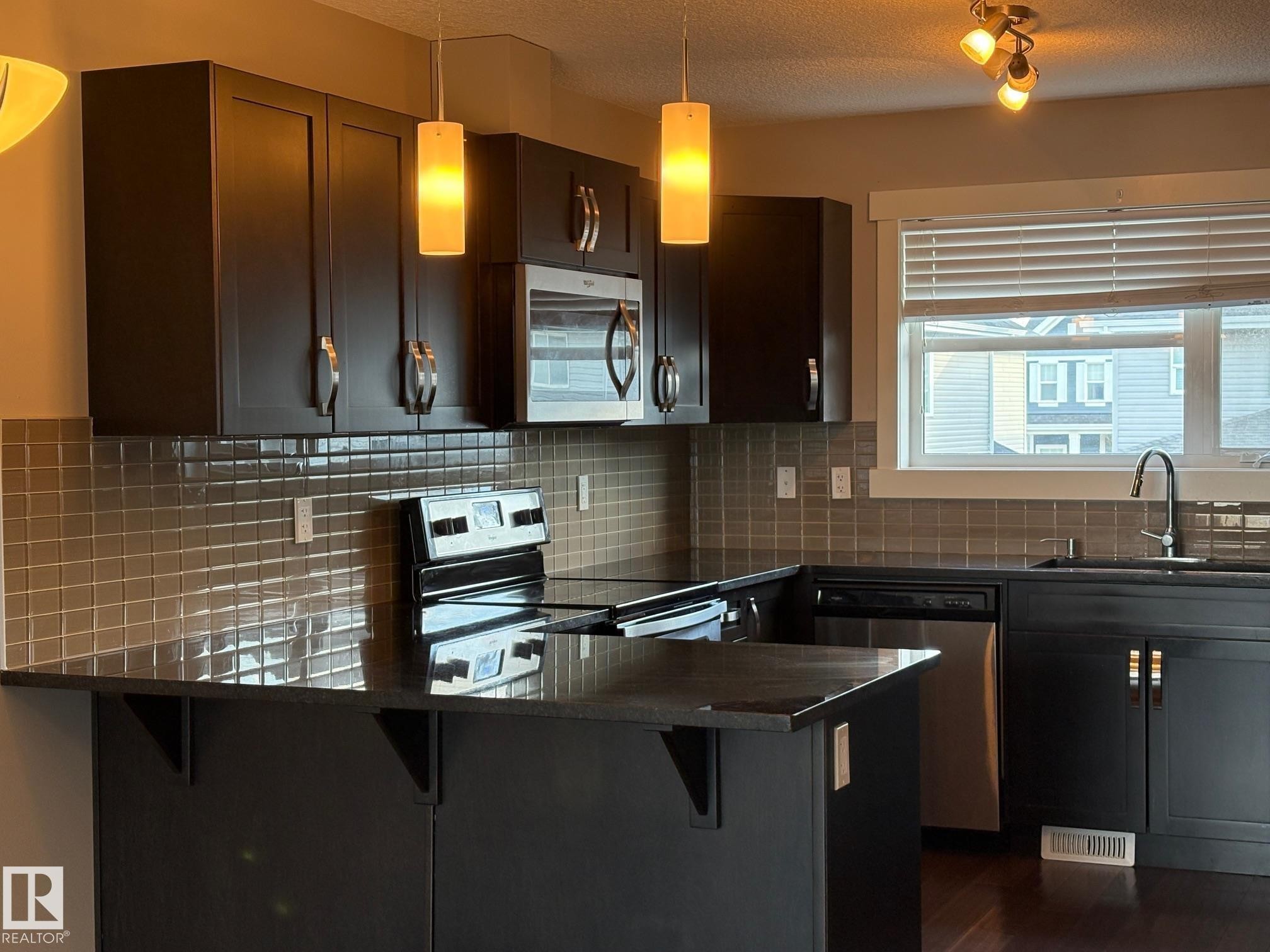 Kitchen featuring dark wood-finish cabinetry, stainless steel appliances, a tile backsplash, and a window above the sink - 295 401 Southfork, Leduc, AB - Indoor Photo Showing Kitchen