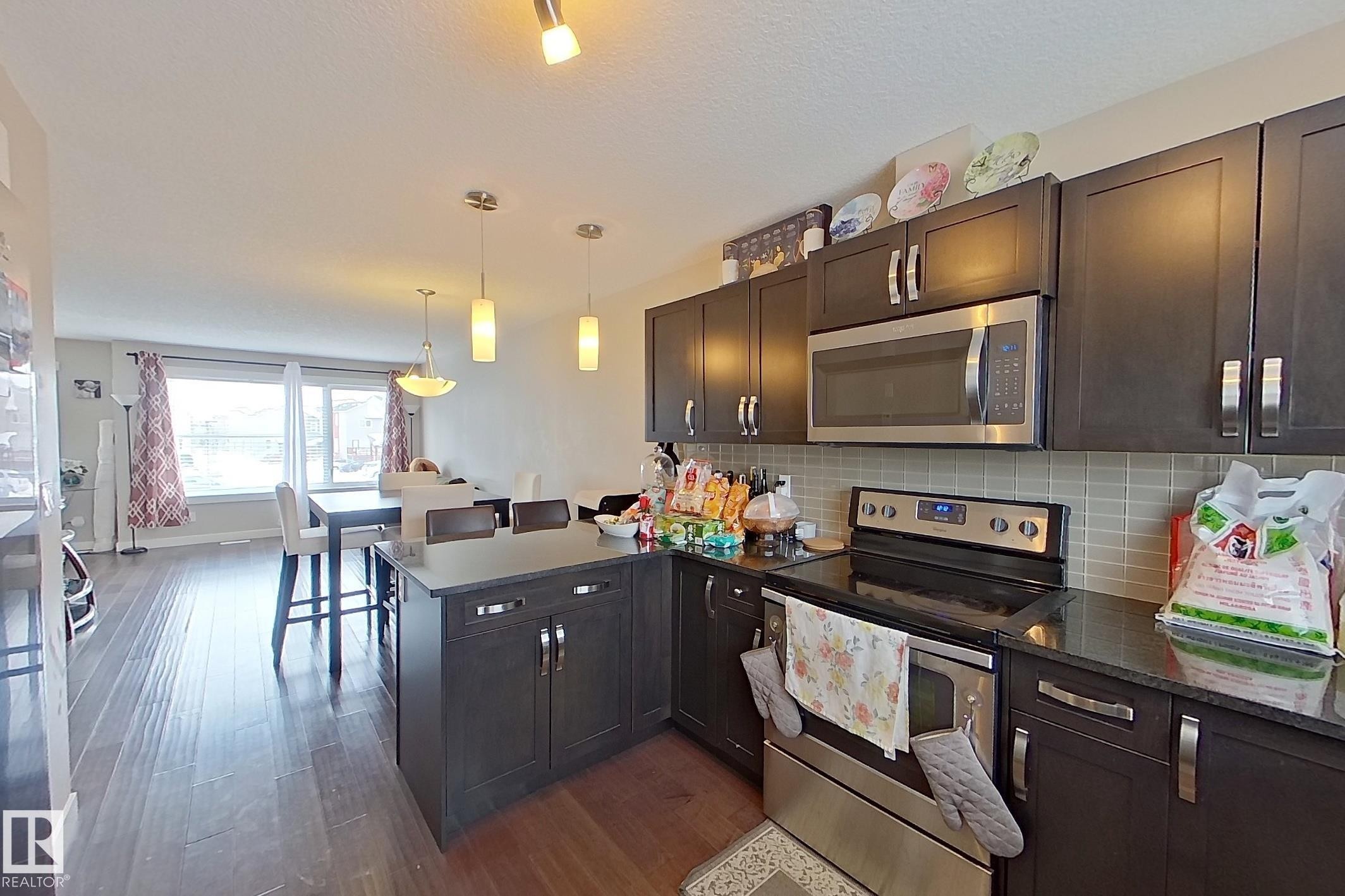 Kitchen featuring dark wood-finish cabinetry, stainless steel appliances, a tile backsplash, and a breakfast bar - 295 401 Southfork, Leduc, AB - Indoor Photo Showing Kitchen With Upgraded Kitchen