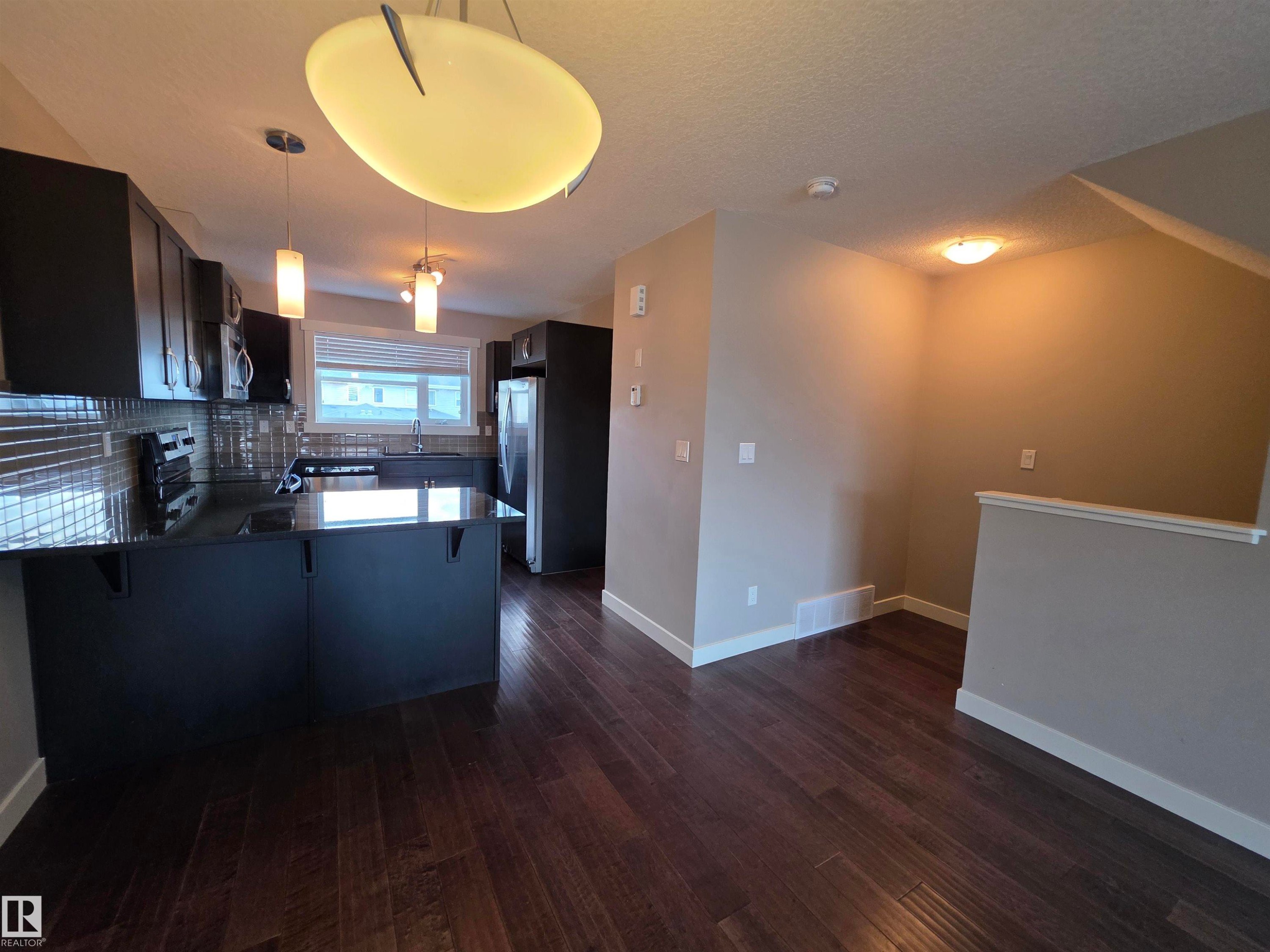 Modern kitchen featuring dark cabinetry, dark countertops, and a full tile backsplash - 295 401 Southfork, Leduc, AB - Indoor Photo Showing Kitchen