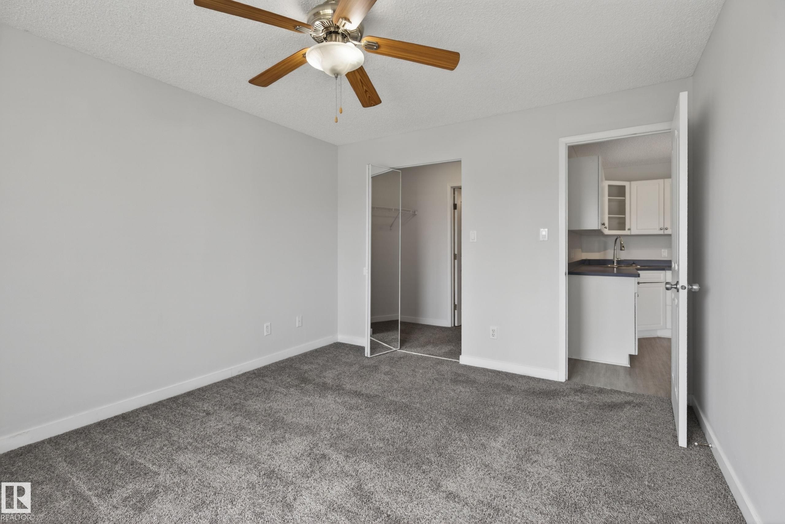Spacious interior room featuring light gray wall paint, gray carpeting, and a ceiling fan with light fixture - #319 16303 95 St Nw, Edmonton, AB - Indoor Photo Showing Other Room